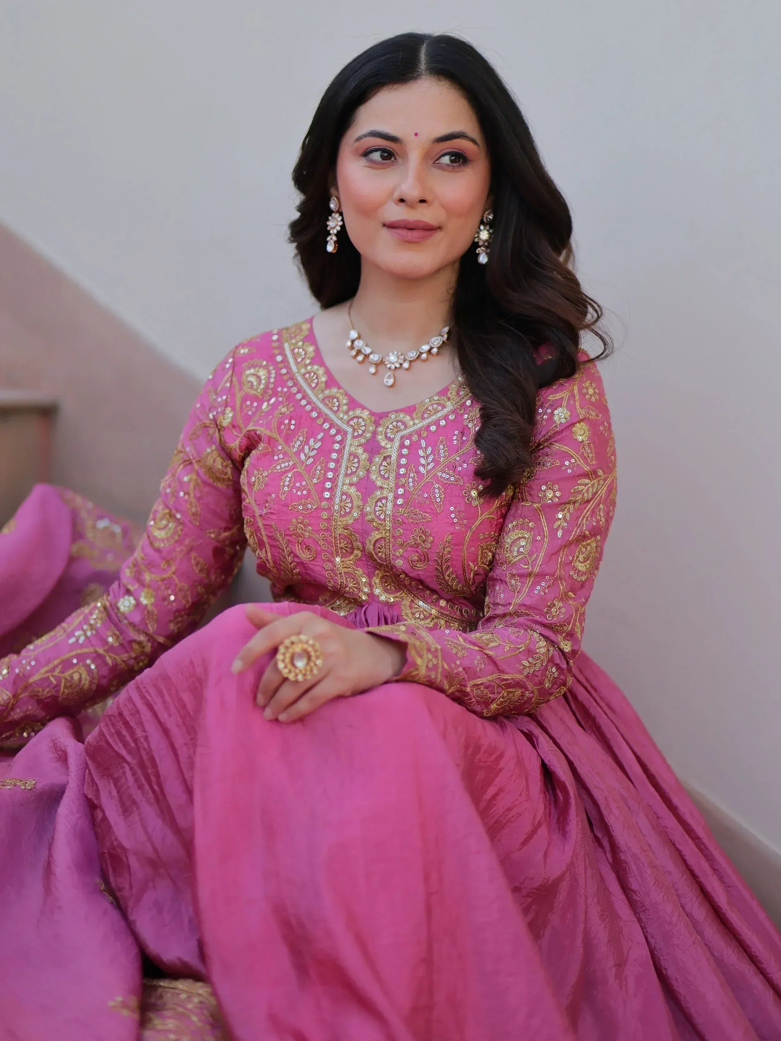 Woman in pink embroidered ethnic gown with gold detailing and traditional jewelry