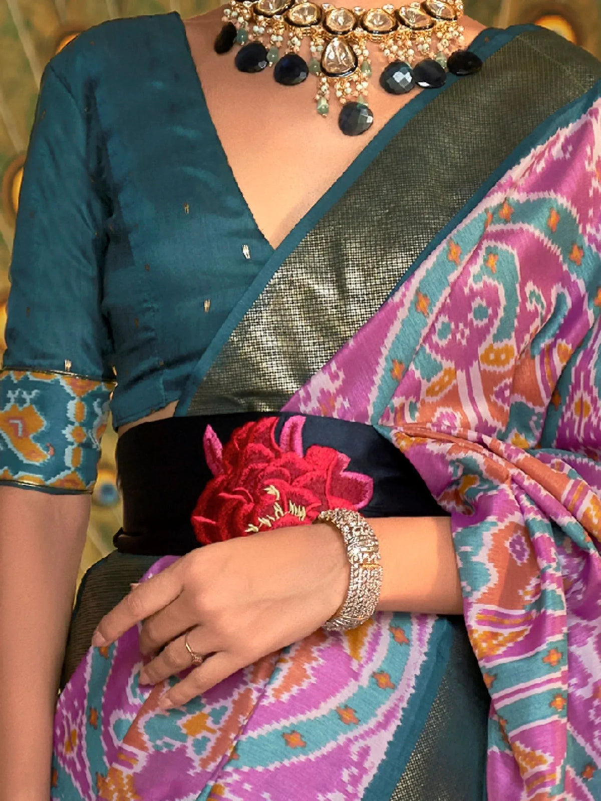 Vibrant ikat saree with teal blouse, floral belt, and statement necklace for Indian ethnic wear