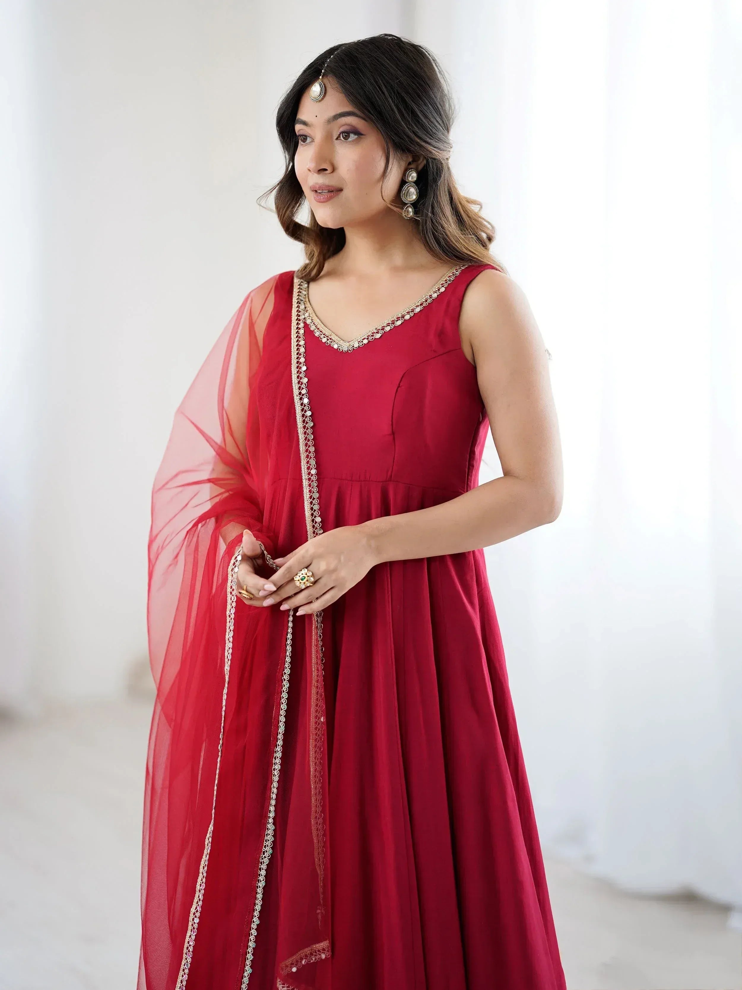 Woman in red ethnic gown with gold embroidery and sheer dupatta, styled with traditional jewelry