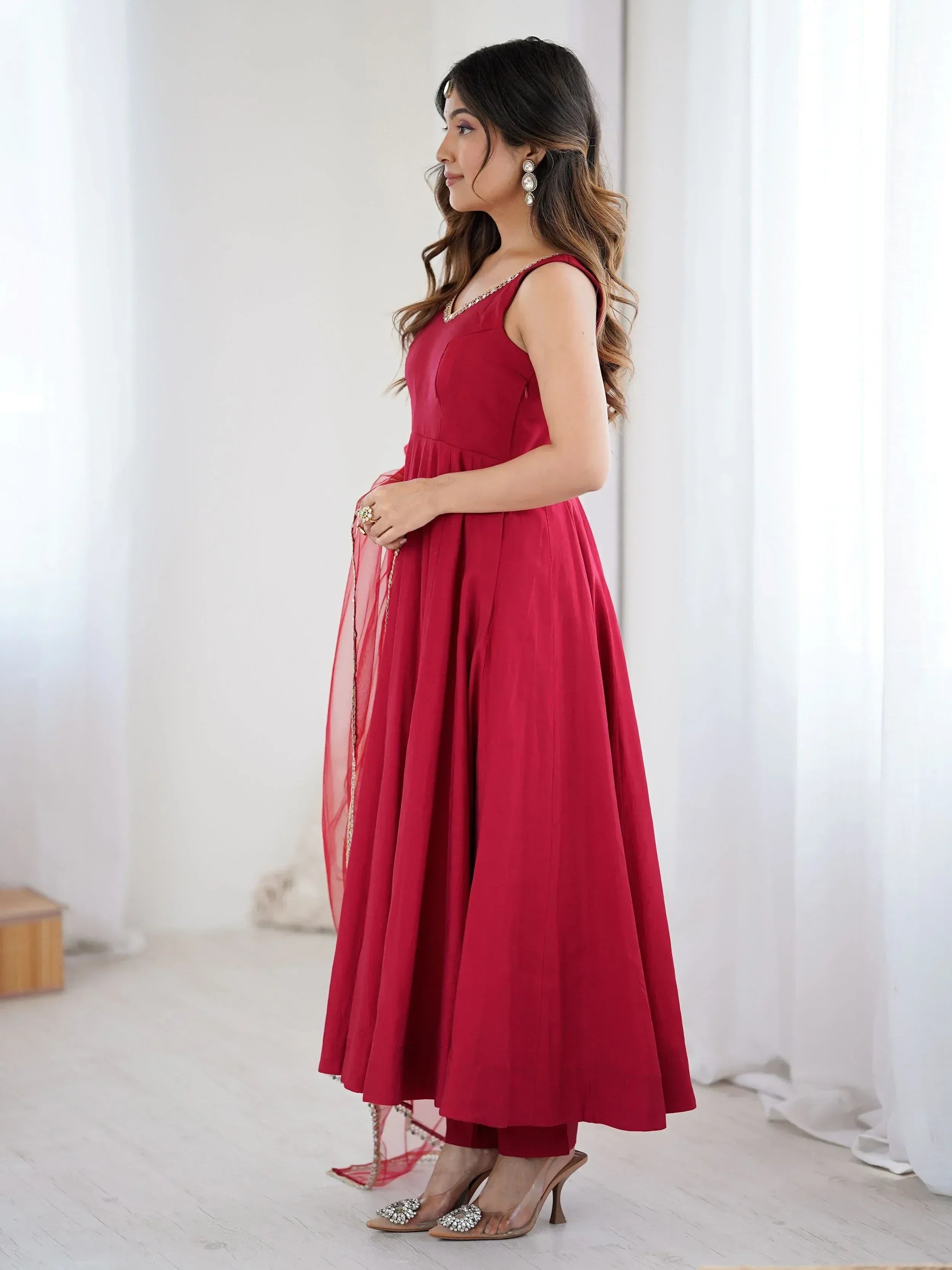 Woman in maroon ethnic gown with gold trim, matching dupatta, and statement earrings for festive occasions