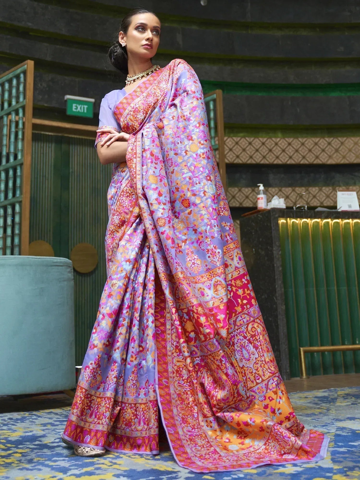 Woman in vibrant floral print saree with pink, purple, and orange hues, styled with gold jewelry for ethnic occasions