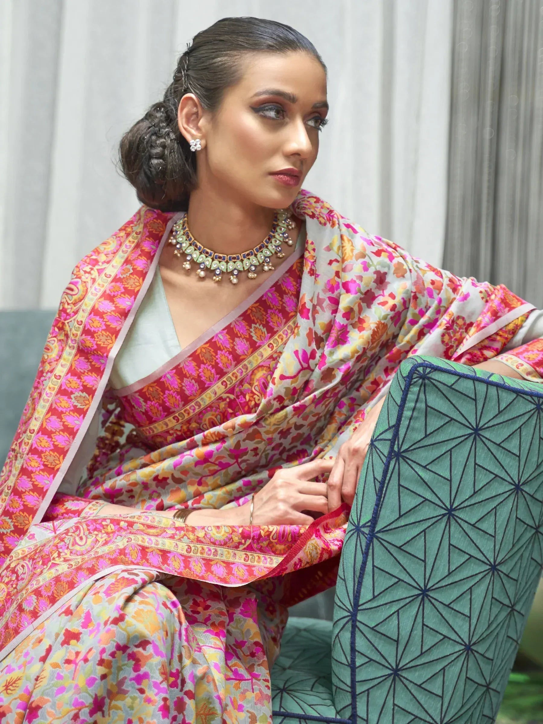 Woman in vibrant floral saree with intricate border, styled with traditional jewelry for ethnic occasions