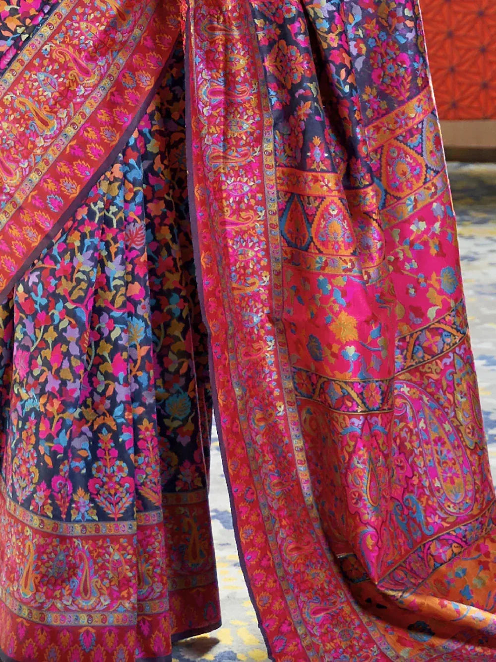 Vibrant Indian ethnic saree with intricate paisley and floral prints in bold pink, blue, and gold tones.