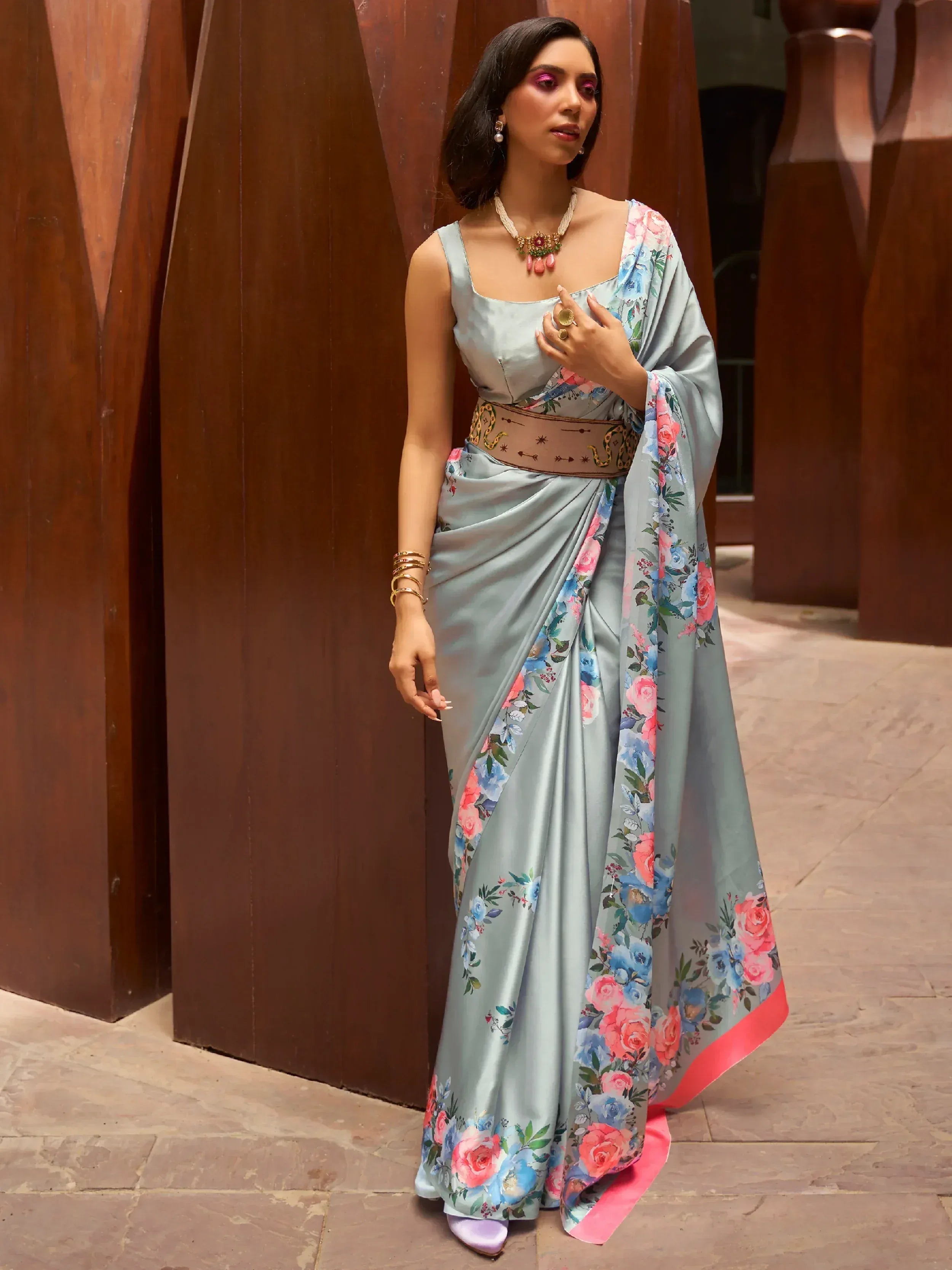 Woman in light blue floral saree with pink border, styled with statement belt and jewelry for ethnic wear