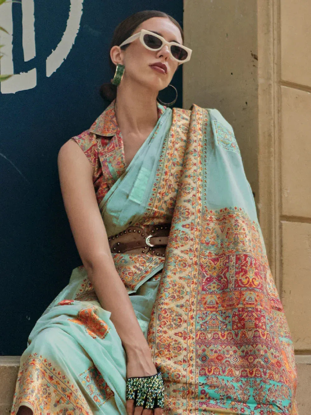 Stylish woman in mint green printed saree with ethnic patterns, modern sunglasses, and statement jewelry