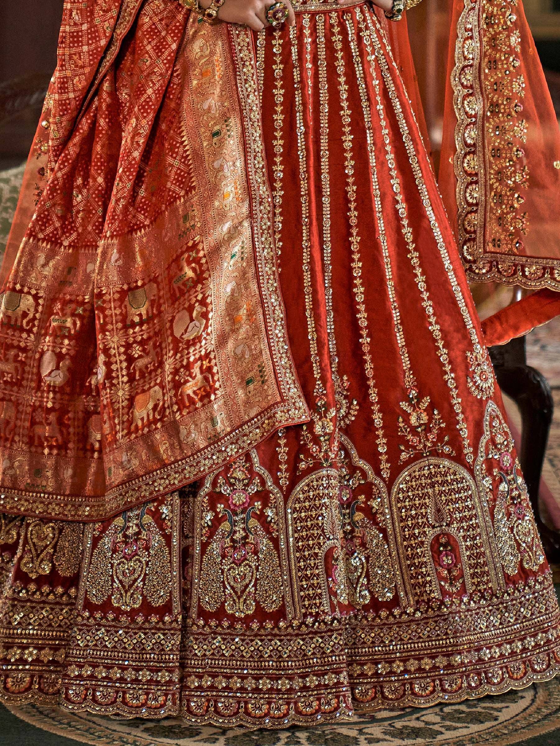 Richly embroidered red velvet lehenga with gold zari, peacock motifs, and intricate border detailing for Indian weddings.