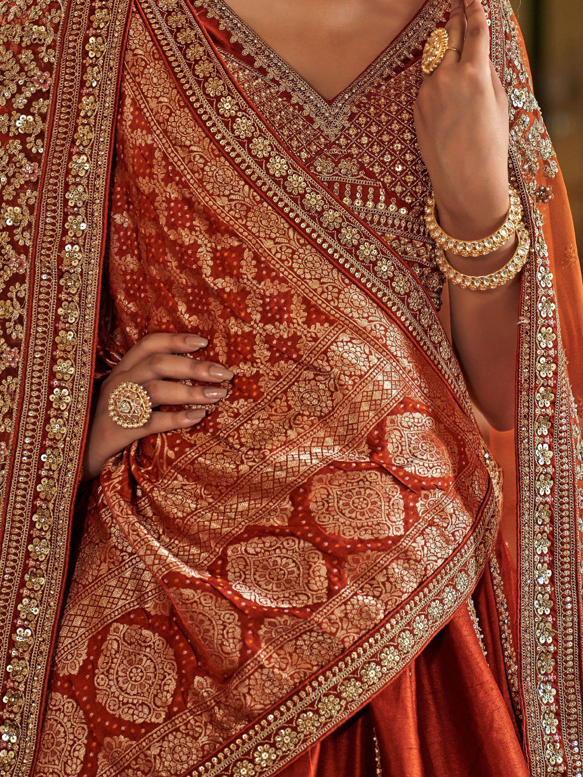 Rich rust orange ethnic saree with gold zari work, sequins, and traditional jewelry for festive occasions