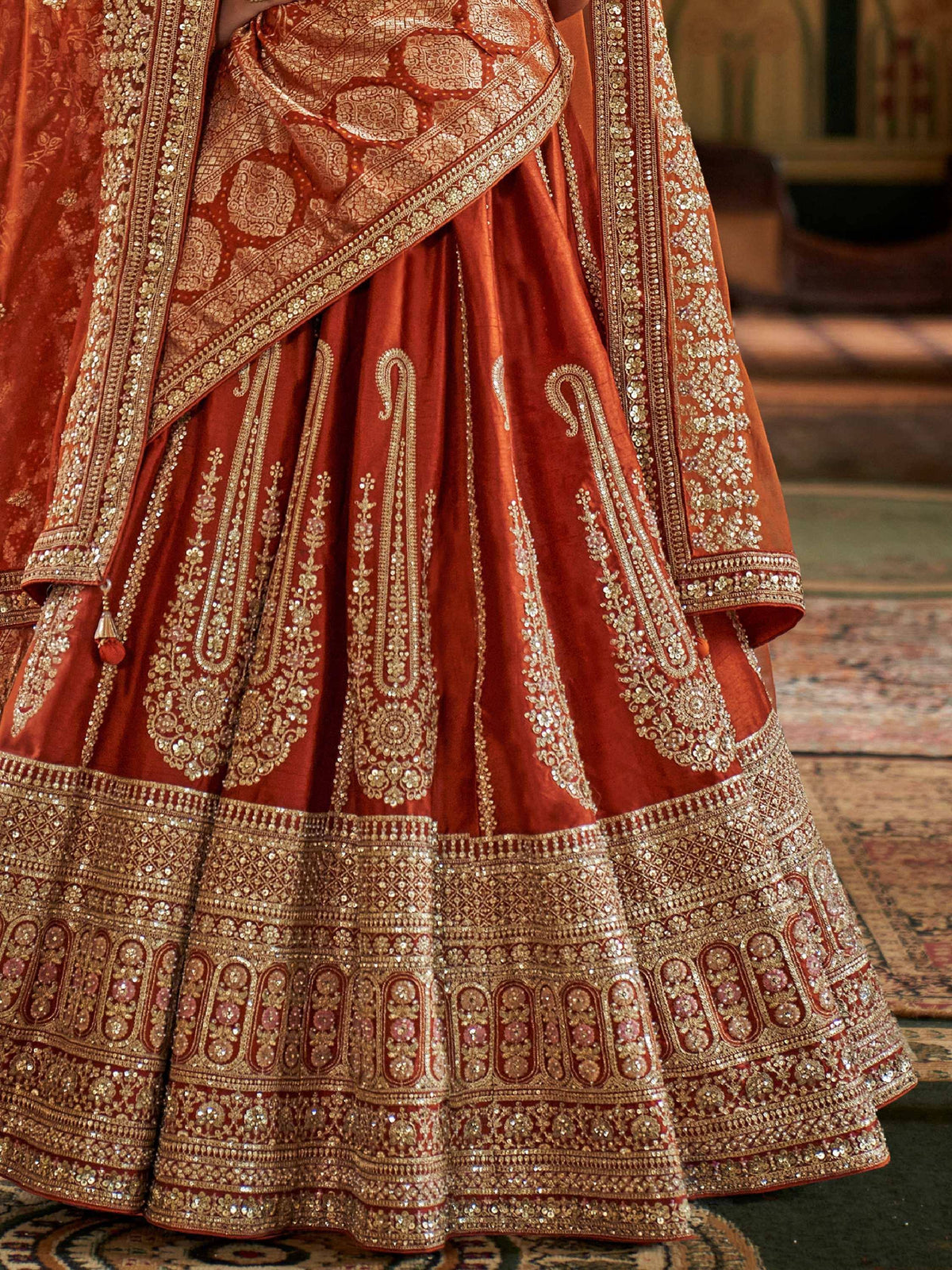 Richly embroidered rust lehenga choli with gold zari work and sequins, perfect for Indian weddings.