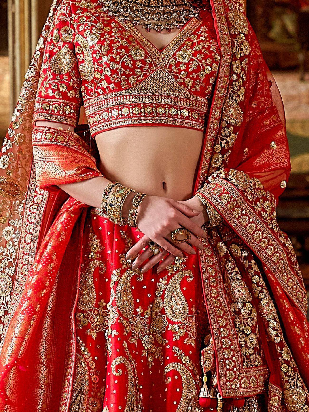 Red and gold embroidered lehenga choli with intricate floral and paisley designs, perfect for Indian weddings.