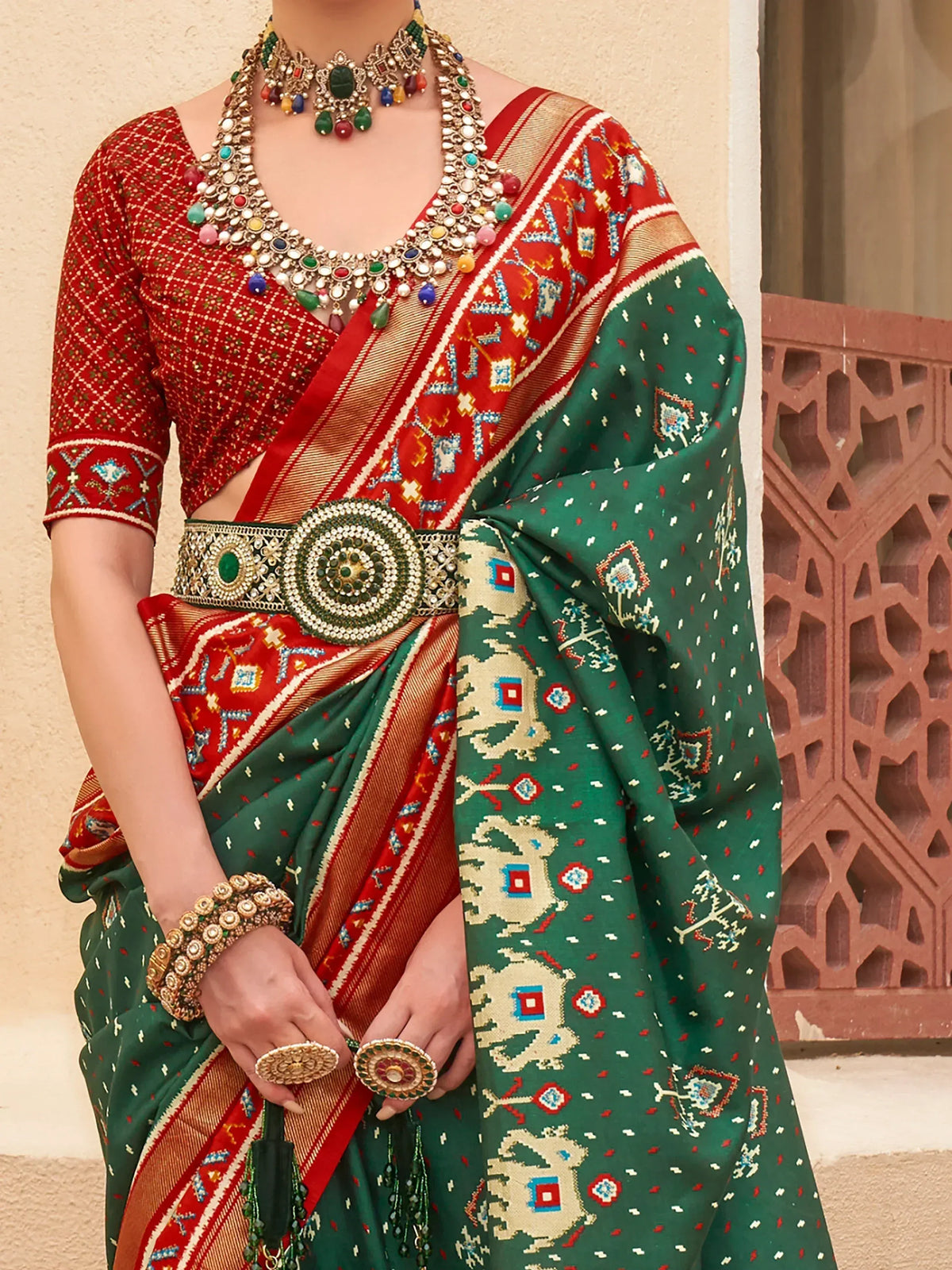 Green and red ethnic saree with intricate embroidery, paired with statement jewelry and a decorative belt.