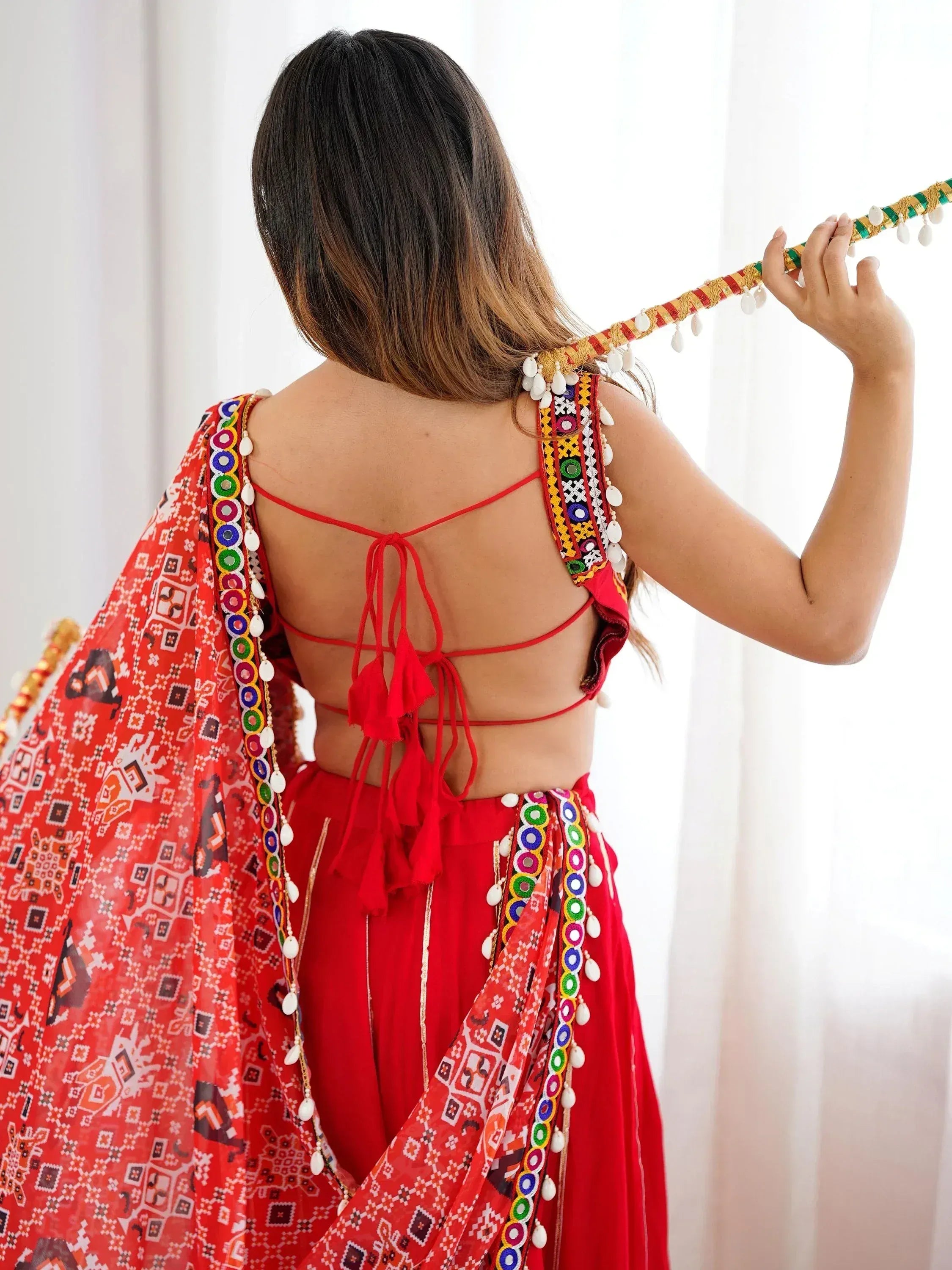 Red ethnic lehenga choli with mirror work, tassels, and printed dupatta for festive occasions