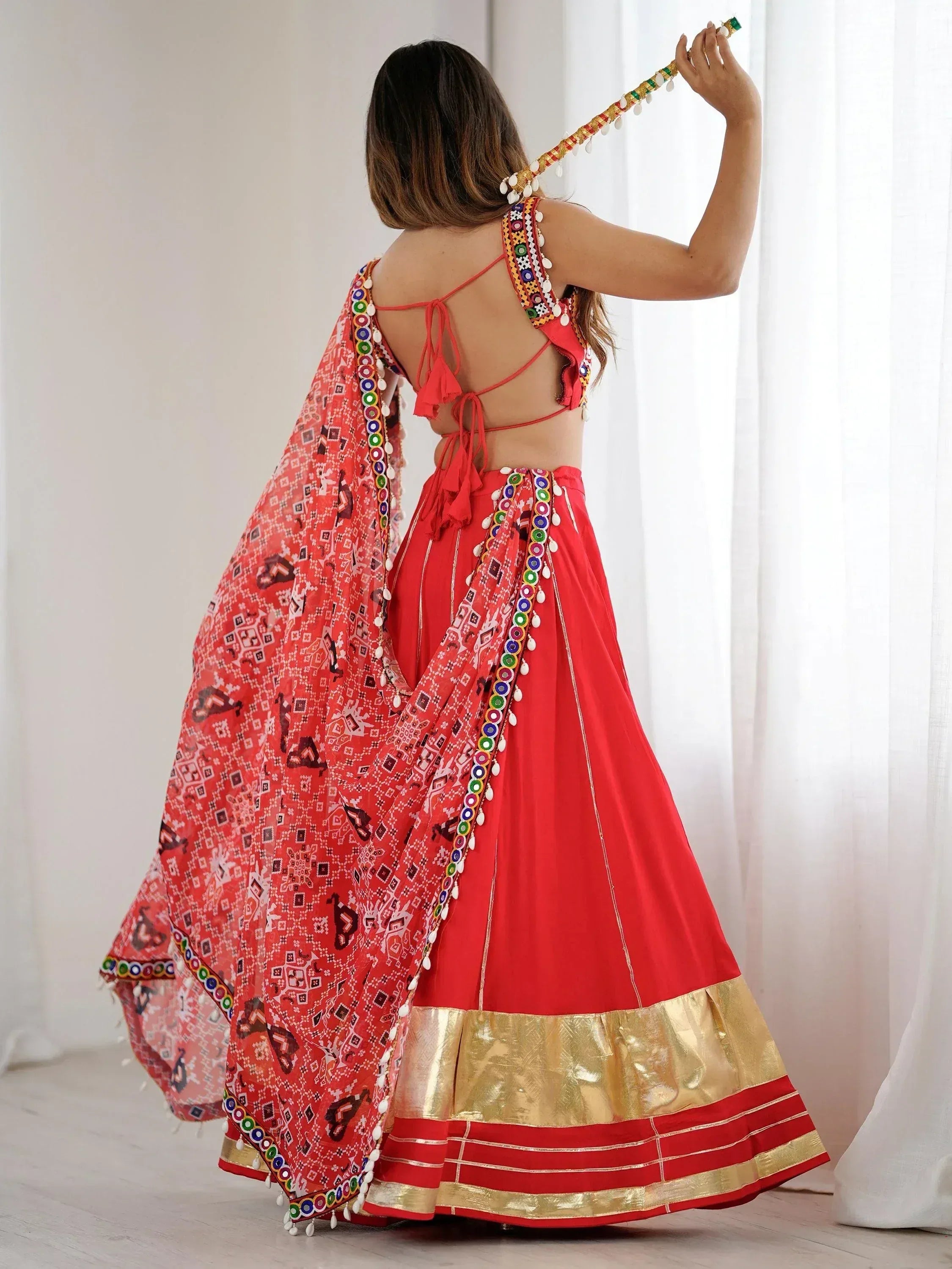 Red ethnic lehenga choli with mirror work, gold border, and printed dupatta for festive occasions