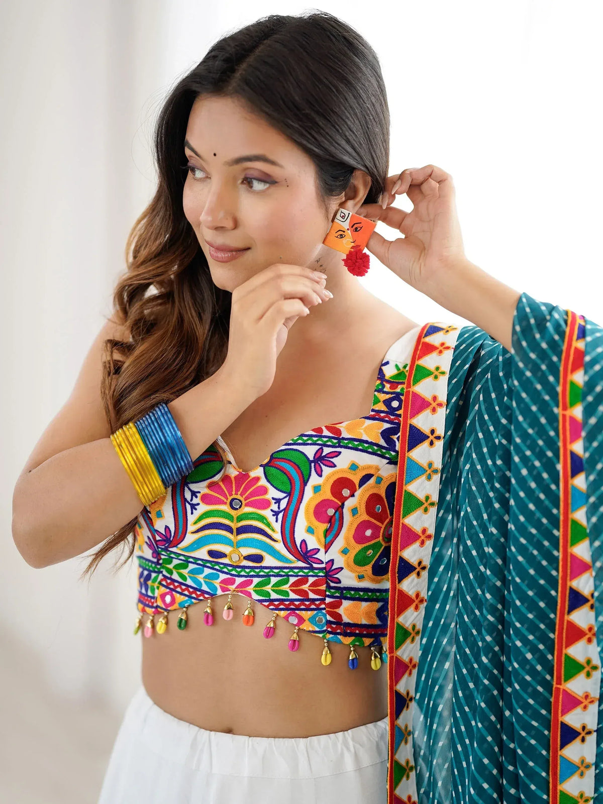 Woman in colorful embroidered ethnic top with mirror work, paired with teal dupatta and statement earrings