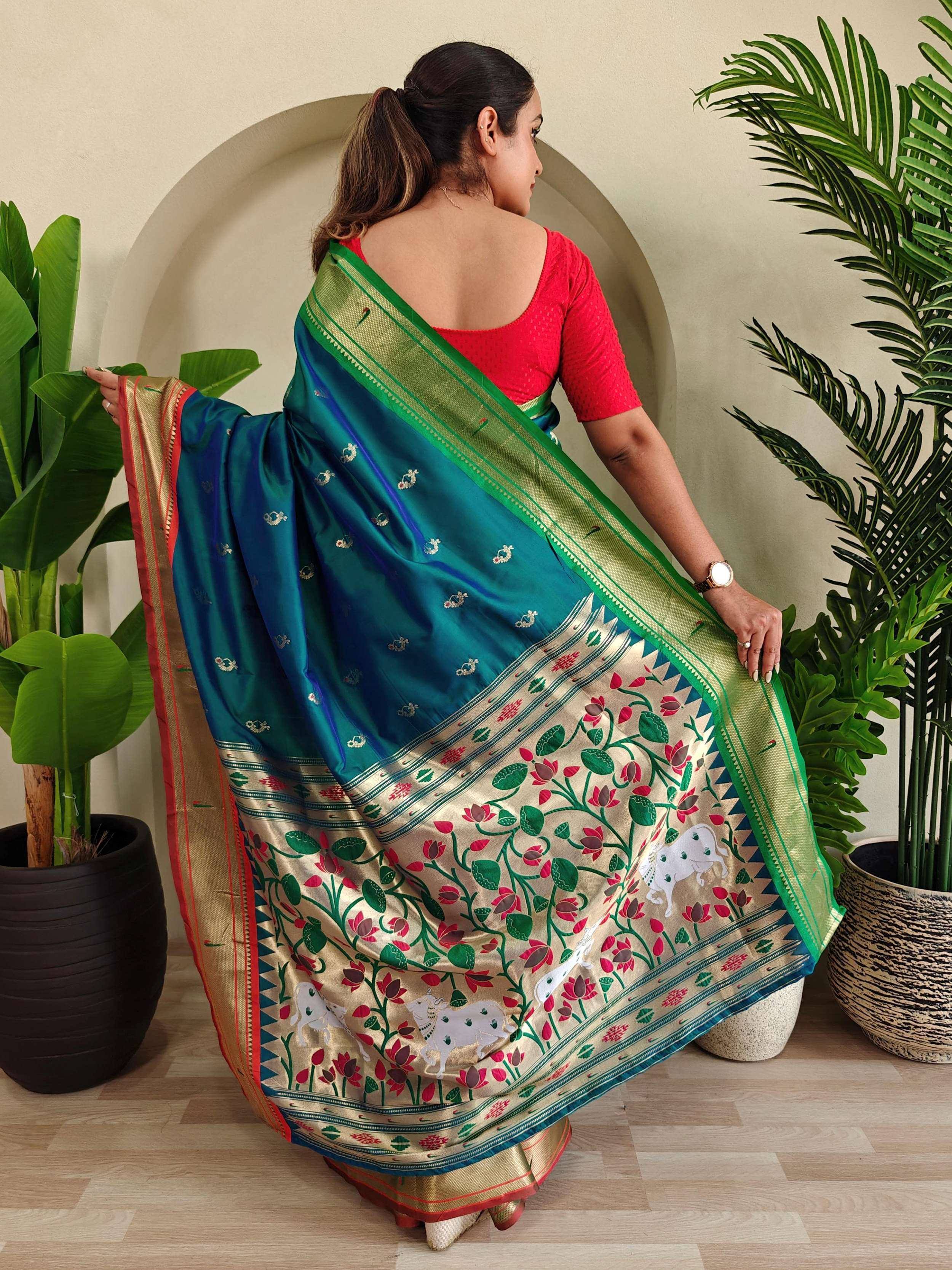 Woman in teal silk saree with floral and cow motifs, red blouse, green border, ethnic Indian wear
