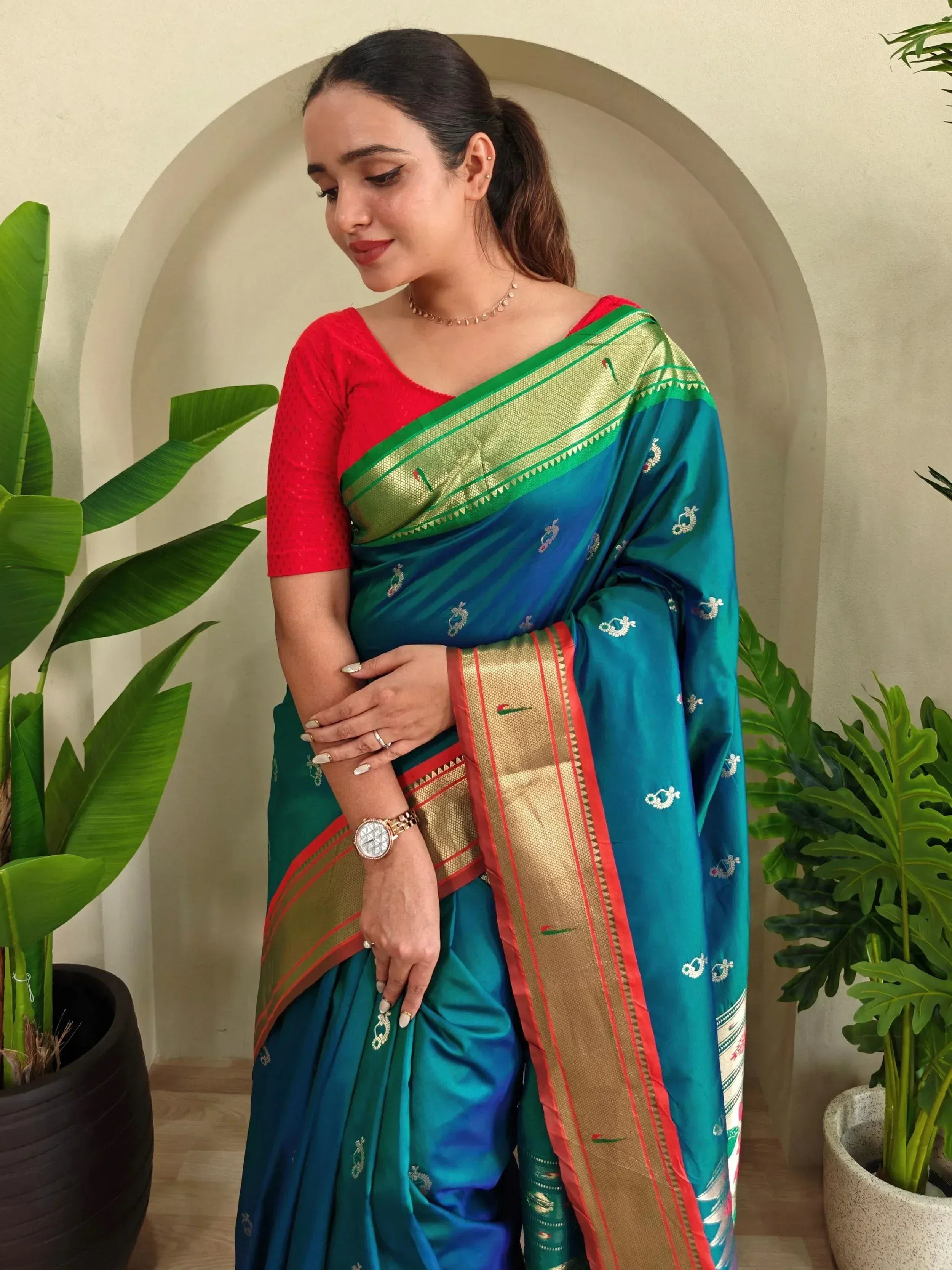 Woman in teal and green designer saree with gold border and red blouse, styled for ethnic occasions