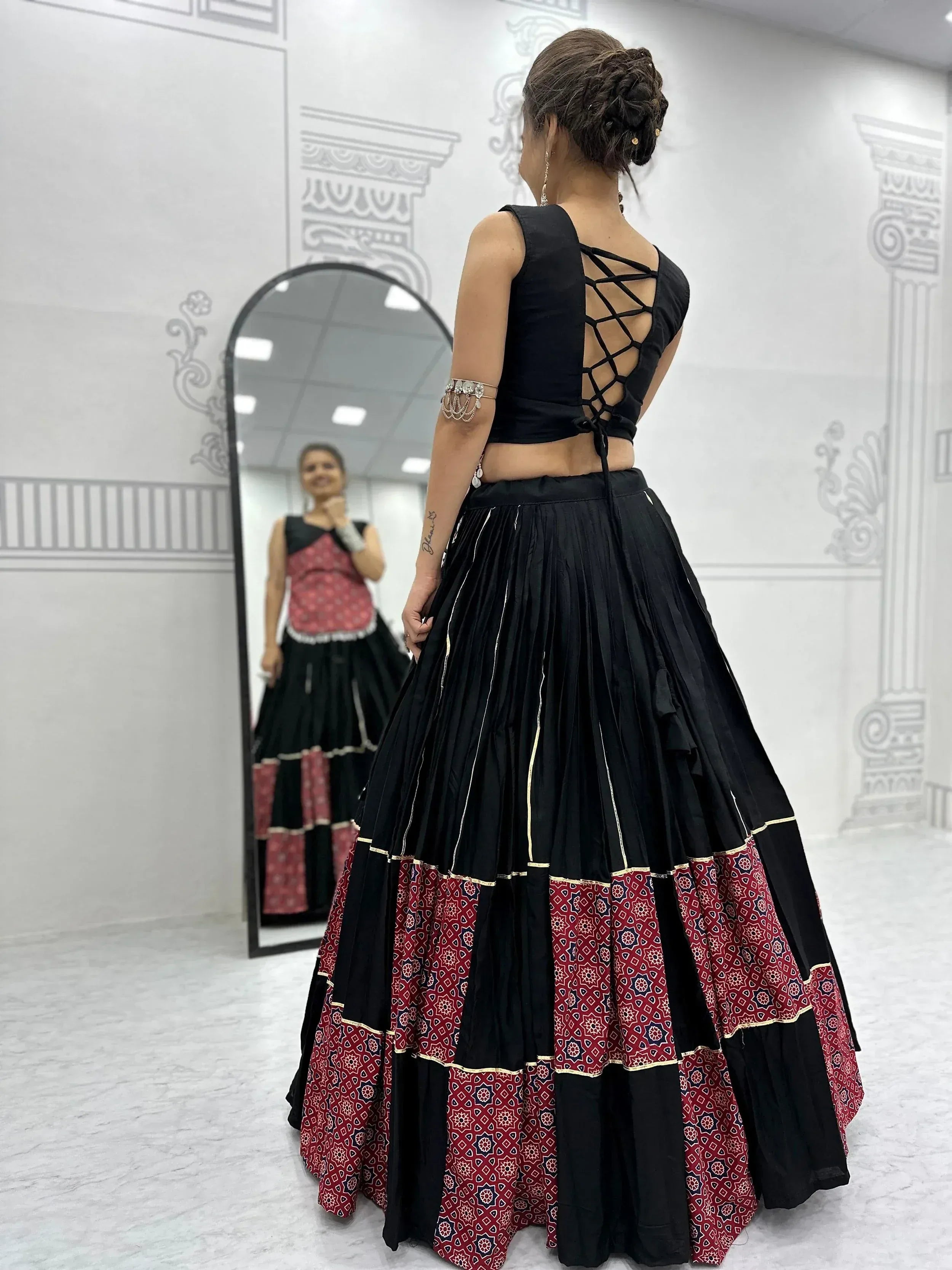 Black and red ethnic lehenga choli with crisscross back blouse and pleated skirt, perfect for Indian weddings or parties.