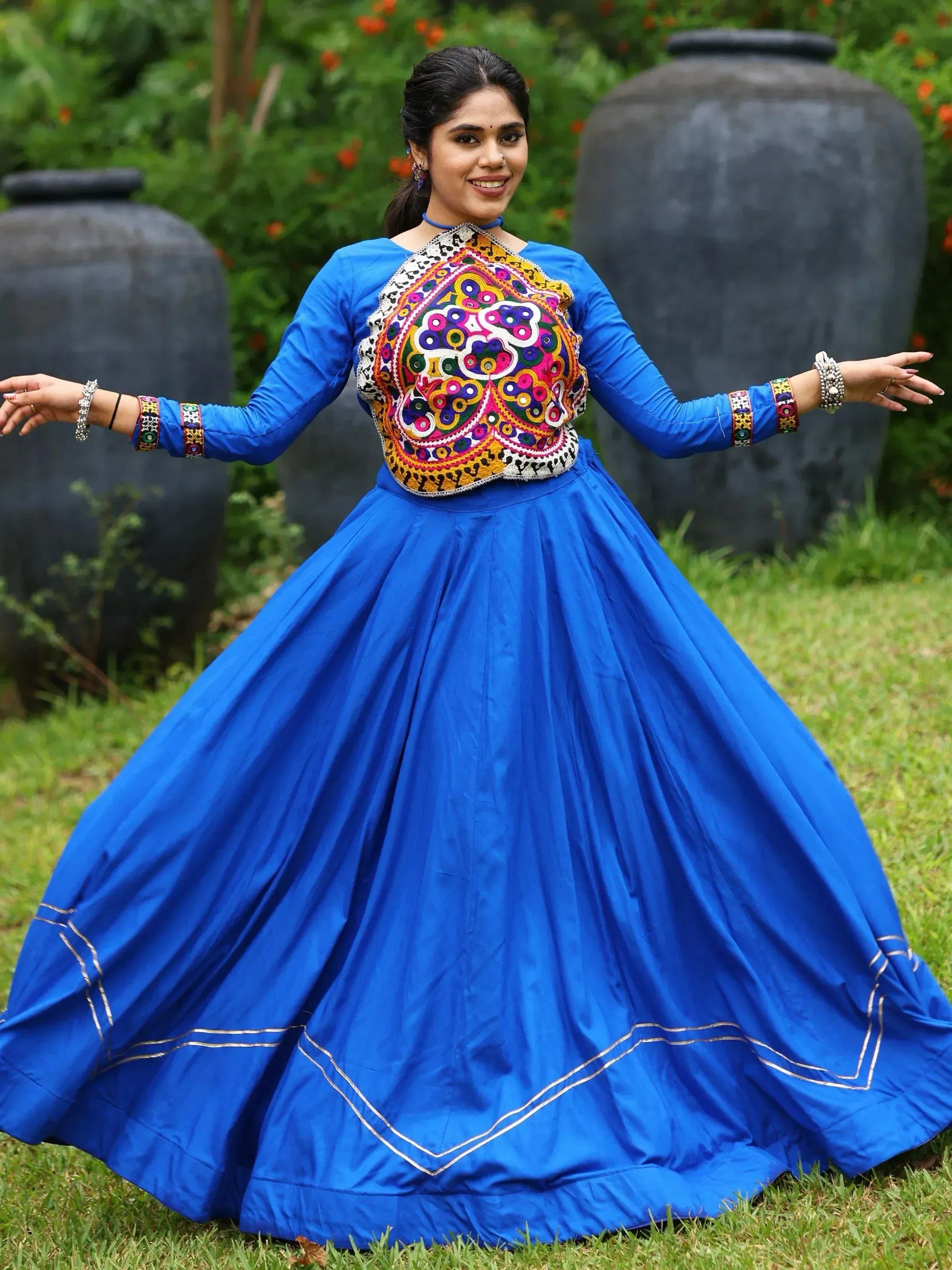 Woman in vibrant blue ethnic gown with colorful mirror work, perfect for Indian festivals and occasions.