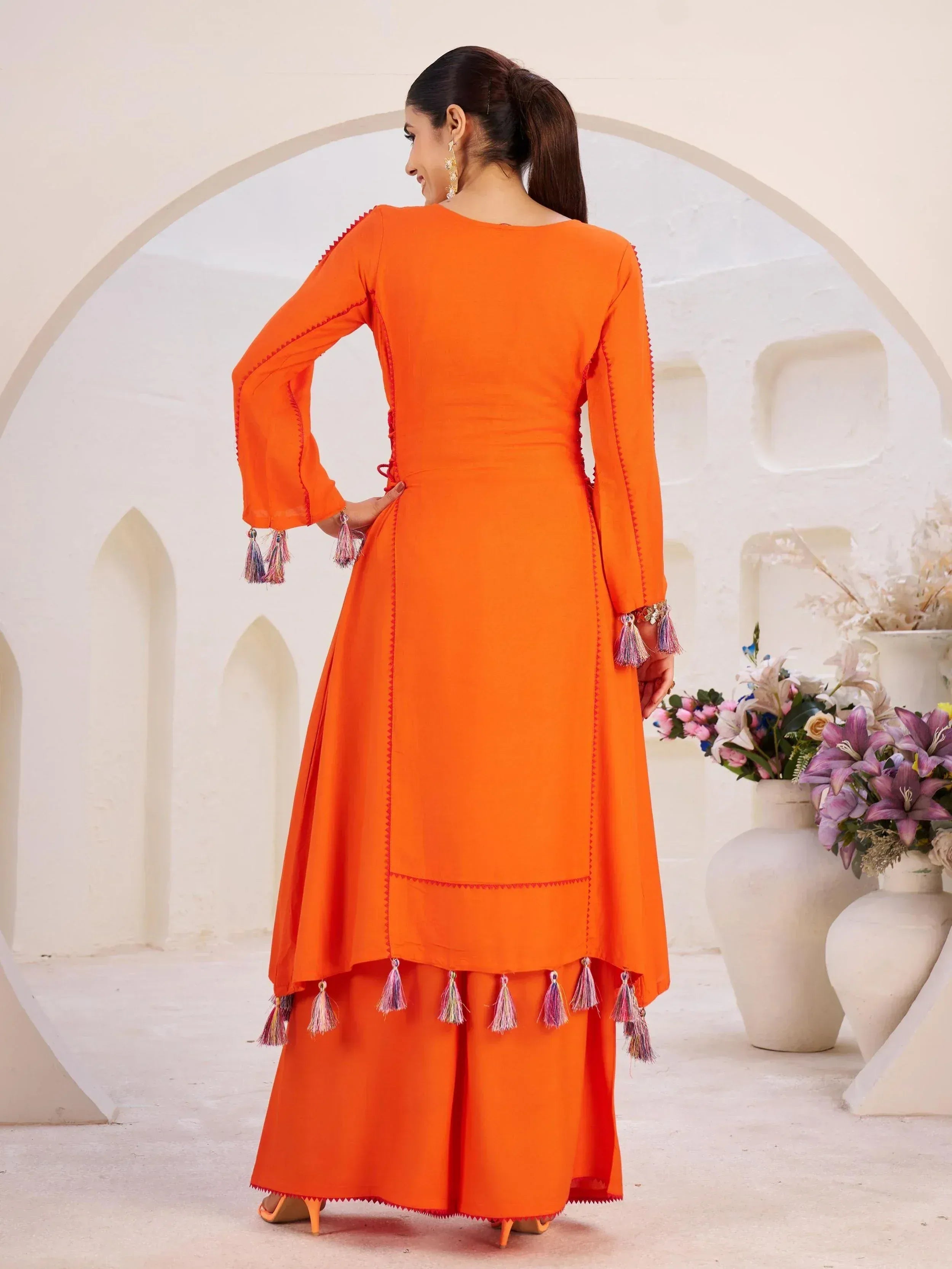 Vibrant orange ethnic gown with tassel detailing, perfect for Indian festive wear and designer occasions.