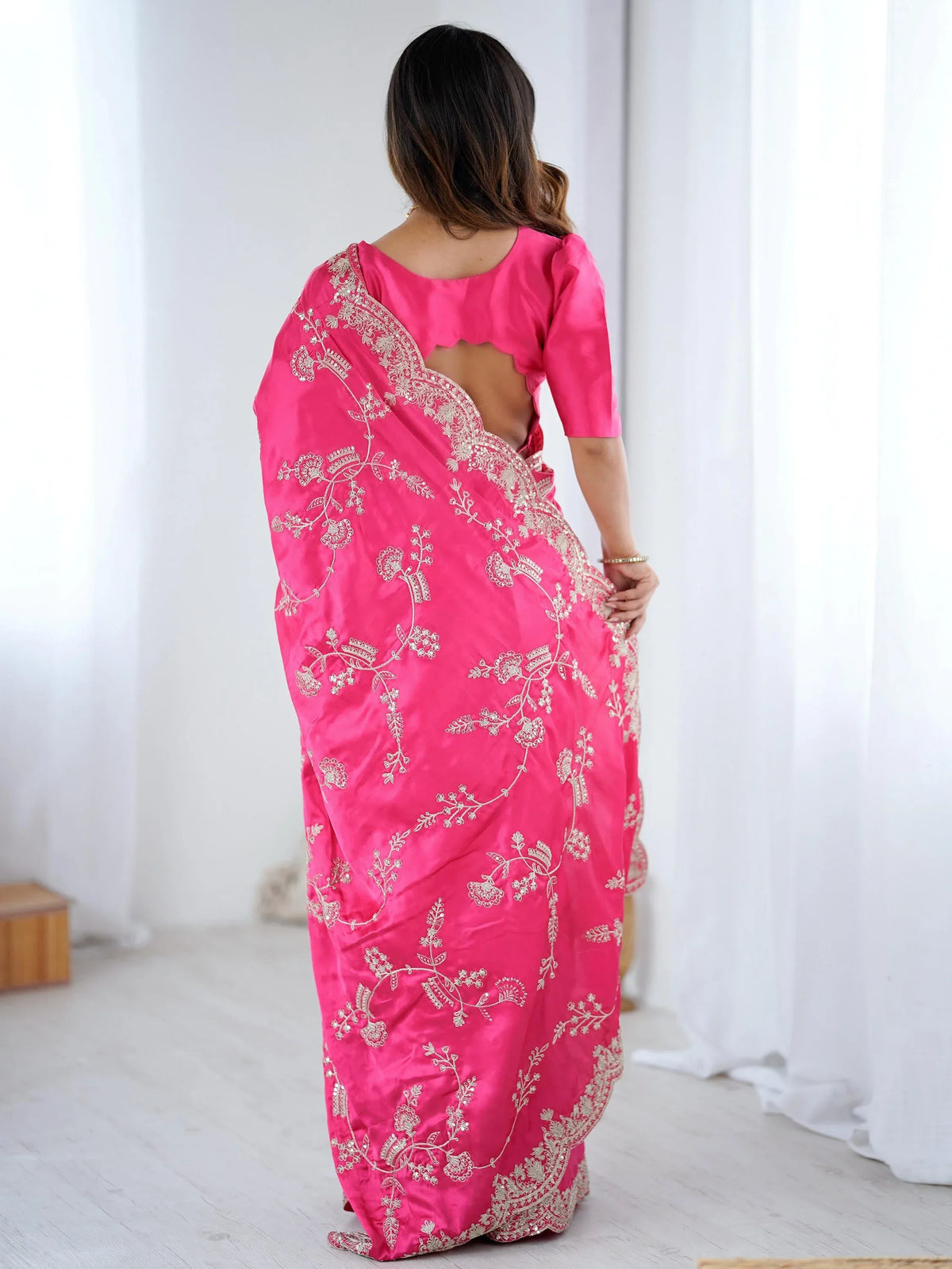 Back view of a woman wearing a pink silk saree with gold embroidery and a matching blouse