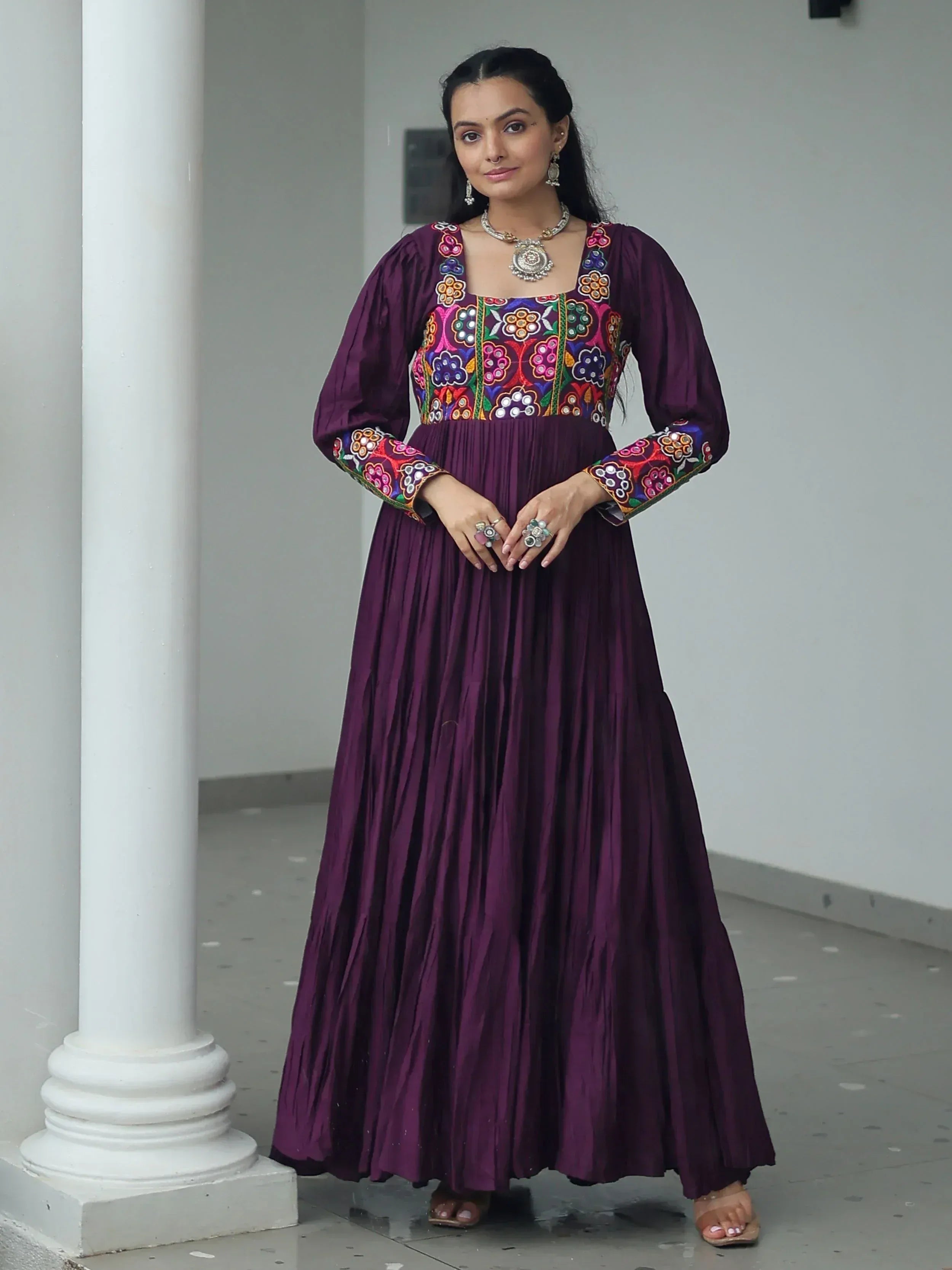 Purple ethnic gown with colorful floral embroidery, pleated skirt, and traditional jewelry for Indian wear