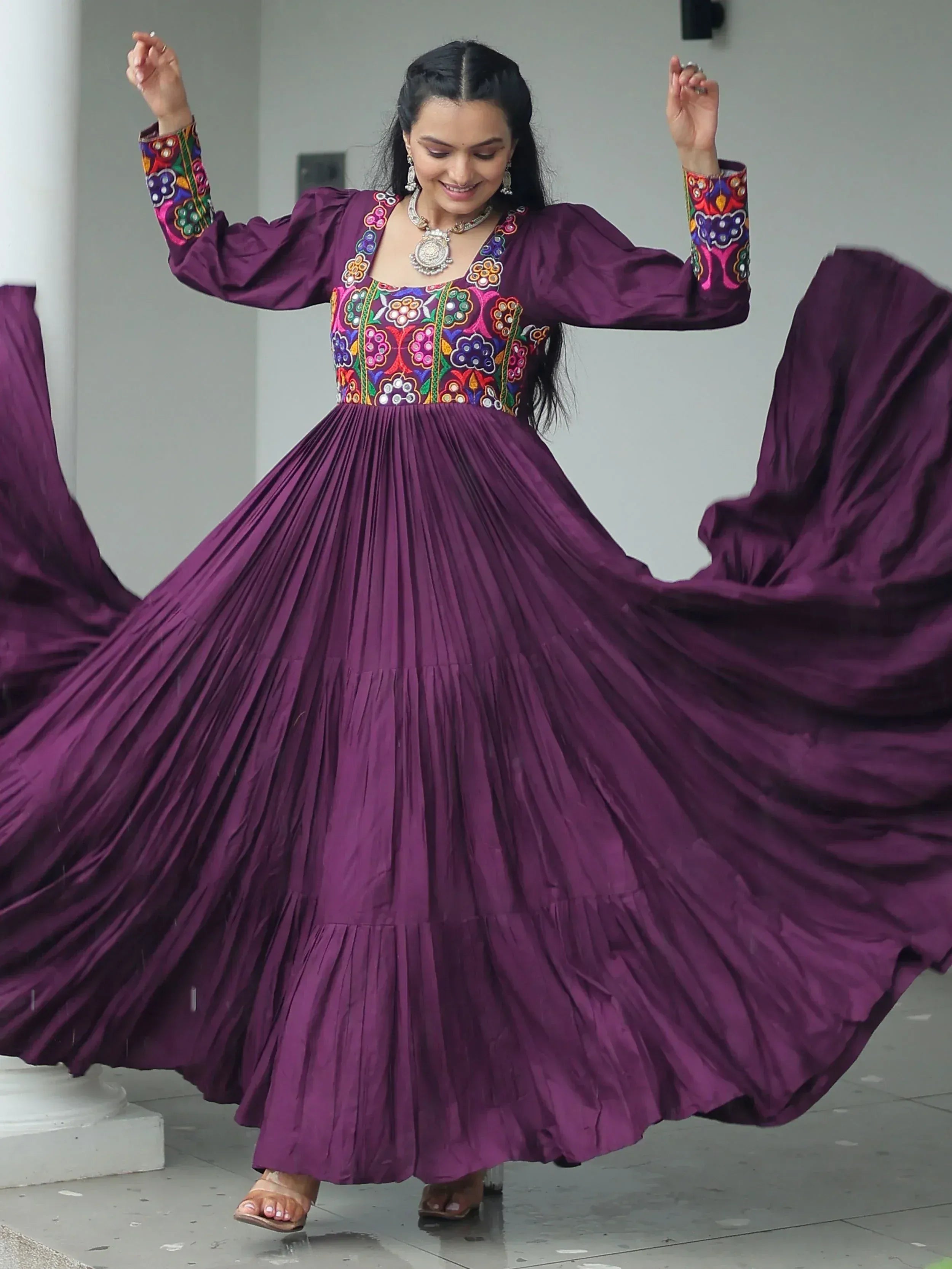Woman twirling in a purple ethnic gown with colorful floral embroidery and pleated skirt