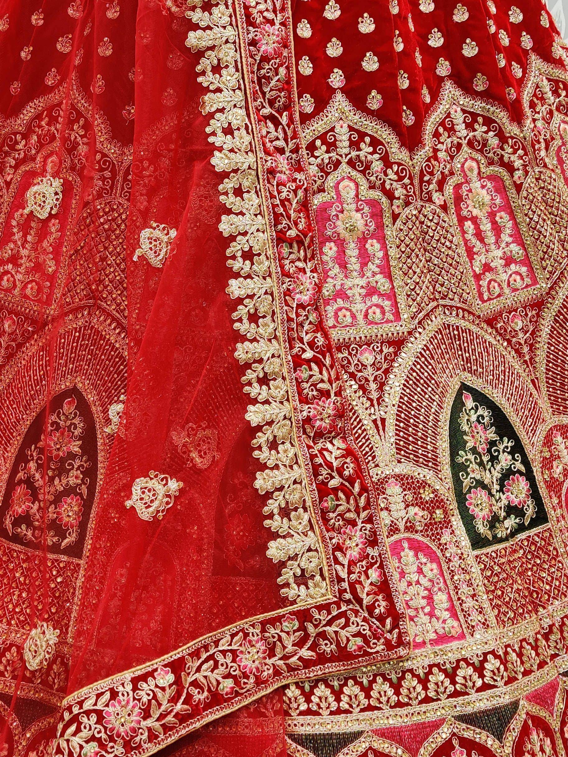 Red velvet lehenga with intricate gold and pink floral embroidery, perfect for Indian weddings.