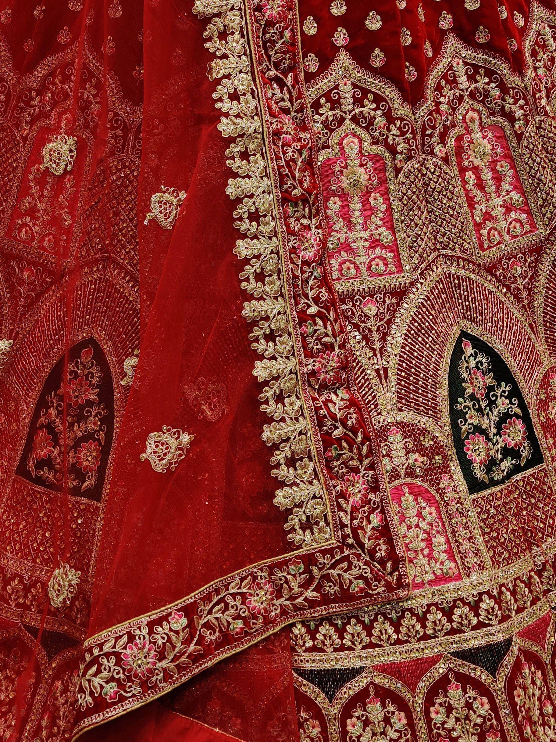 Red velvet lehenga choli with intricate gold and pink floral embroidery, perfect for Indian weddings.