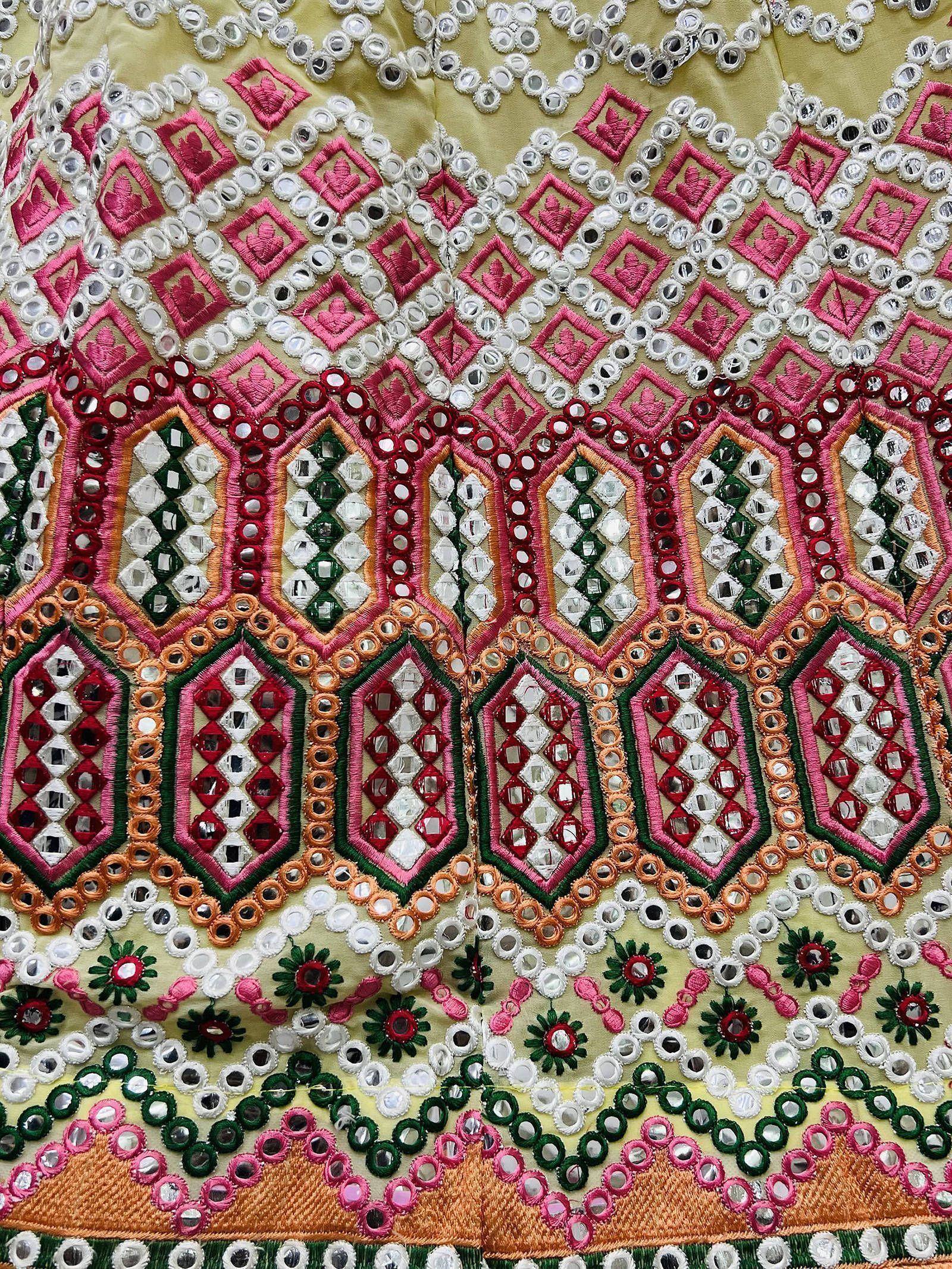Colorful mirror work embroidery on ethnic wear, featuring pink, green, and gold patterns with intricate bead detailing.