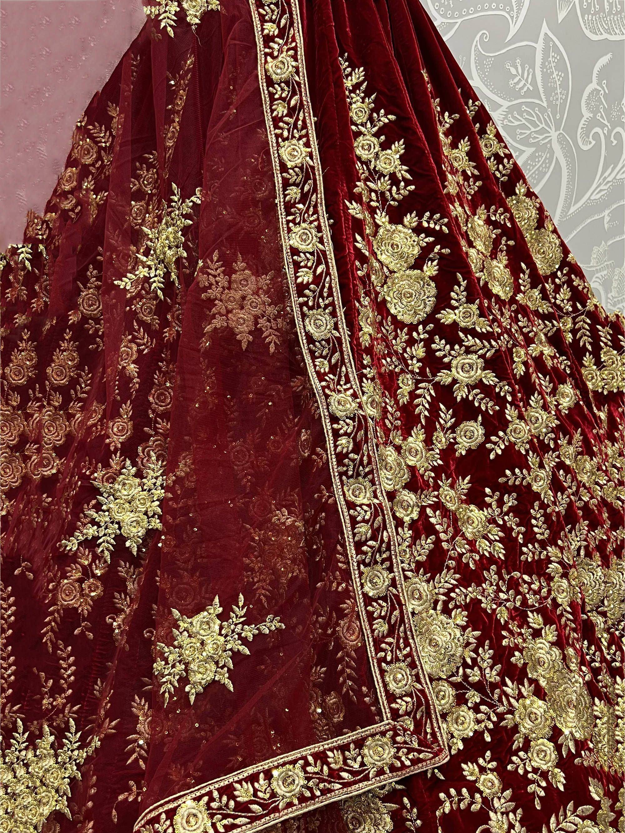 Luxury maroon velvet lehenga with intricate gold floral embroidery and sheer dupatta, perfect for Indian weddings.