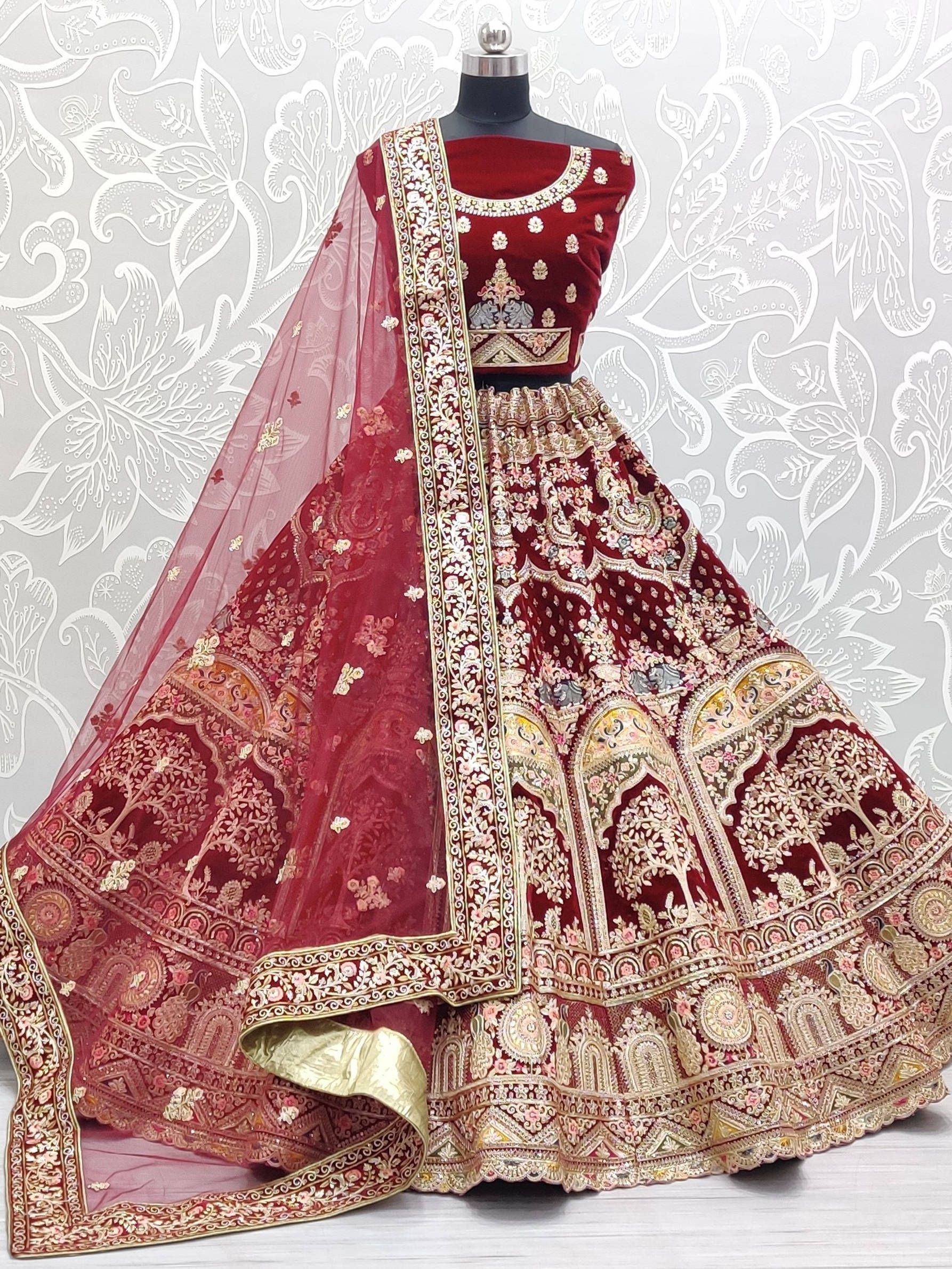 Luxury maroon velvet lehenga choli with heavy gold embroidery and floral dupatta, perfect for Indian weddings.
