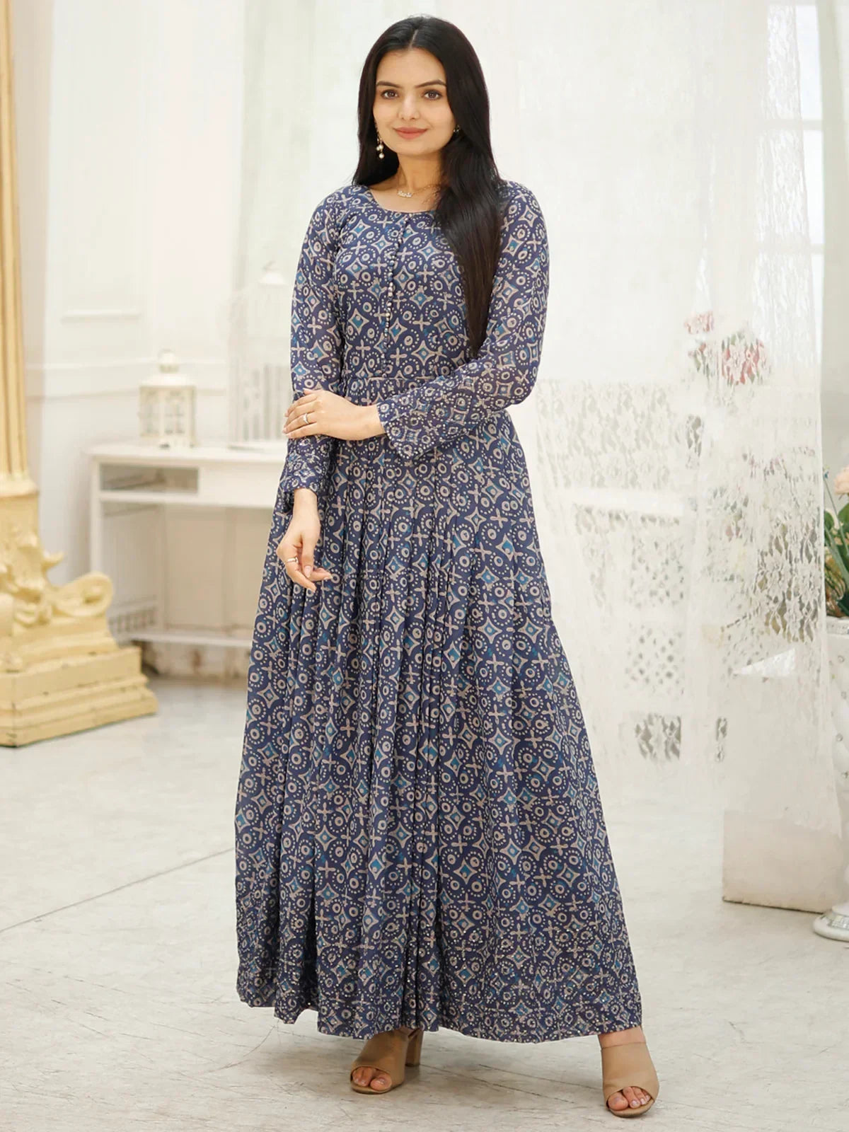 Woman in a blue printed ethnic gown with long sleeves, standing indoors.
