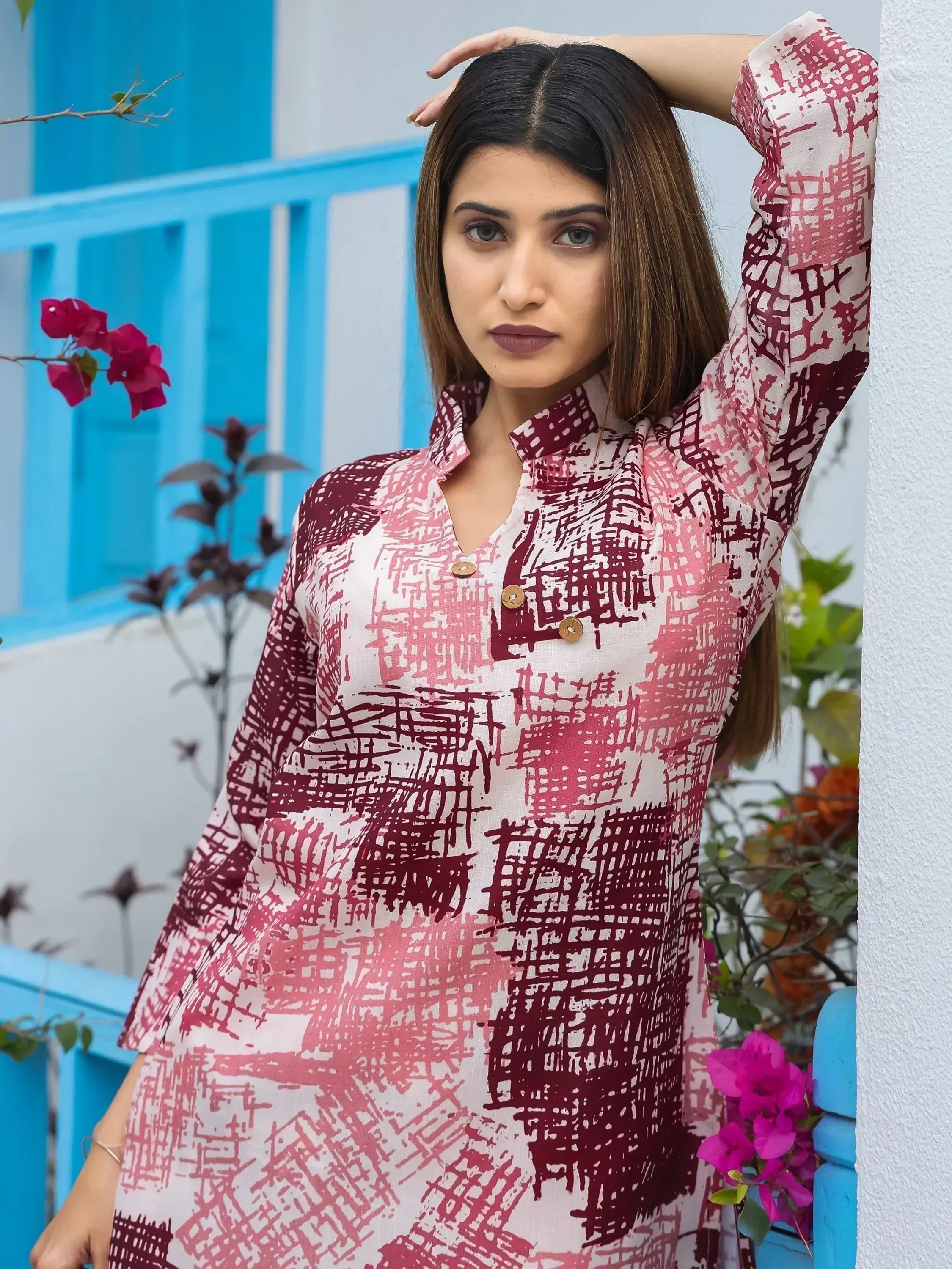 Woman in printed ethnic kurta with maroon and pink abstract design, standing by blue railing