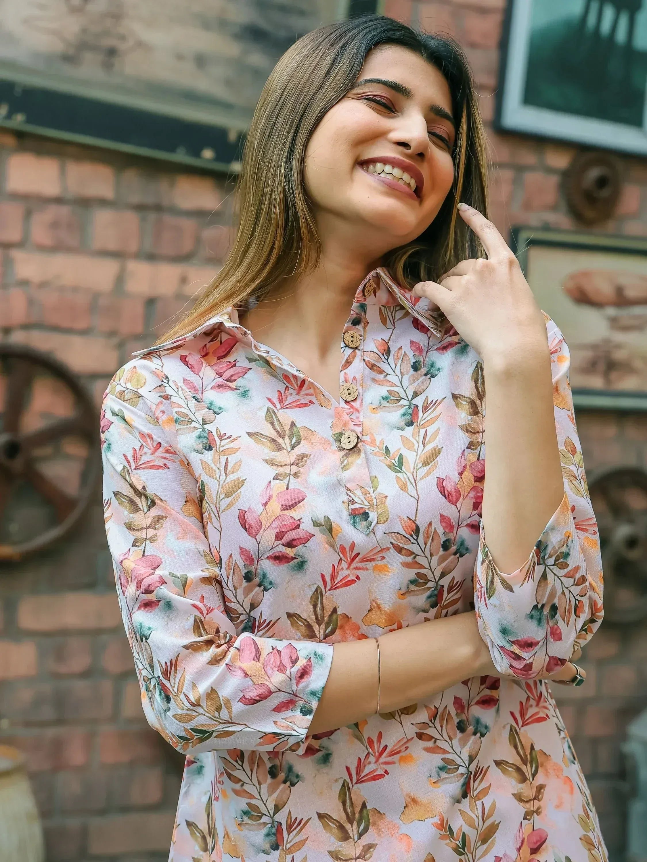 Woman in floral print kurti with three-quarter sleeves, smiling against brick wall backdrop