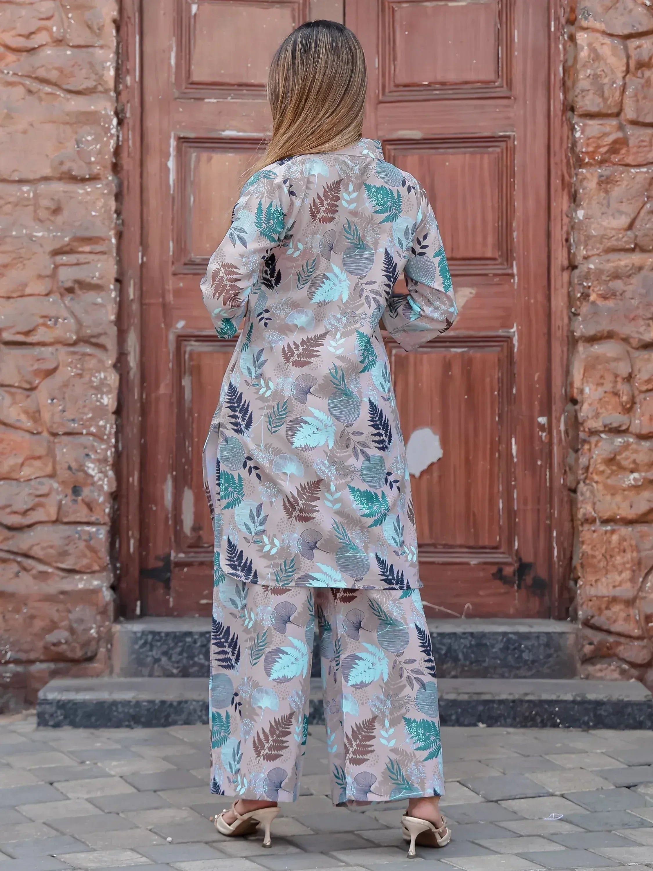 Woman in floral print ethnic kurta and palazzo pants, standing before rustic wooden door