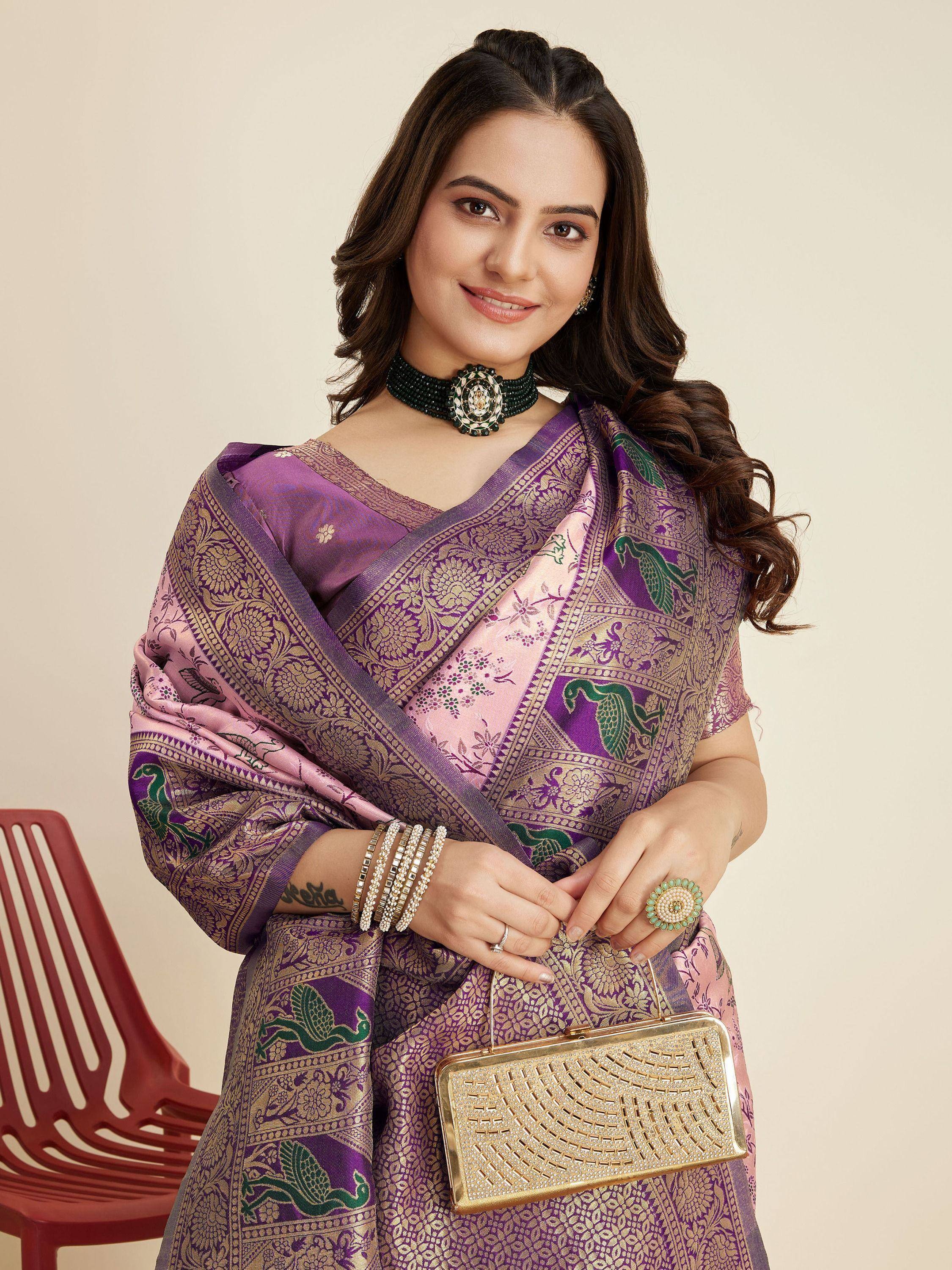 Woman in purple and pink designer saree with peacock print, ethnic jewelry, and gold clutch