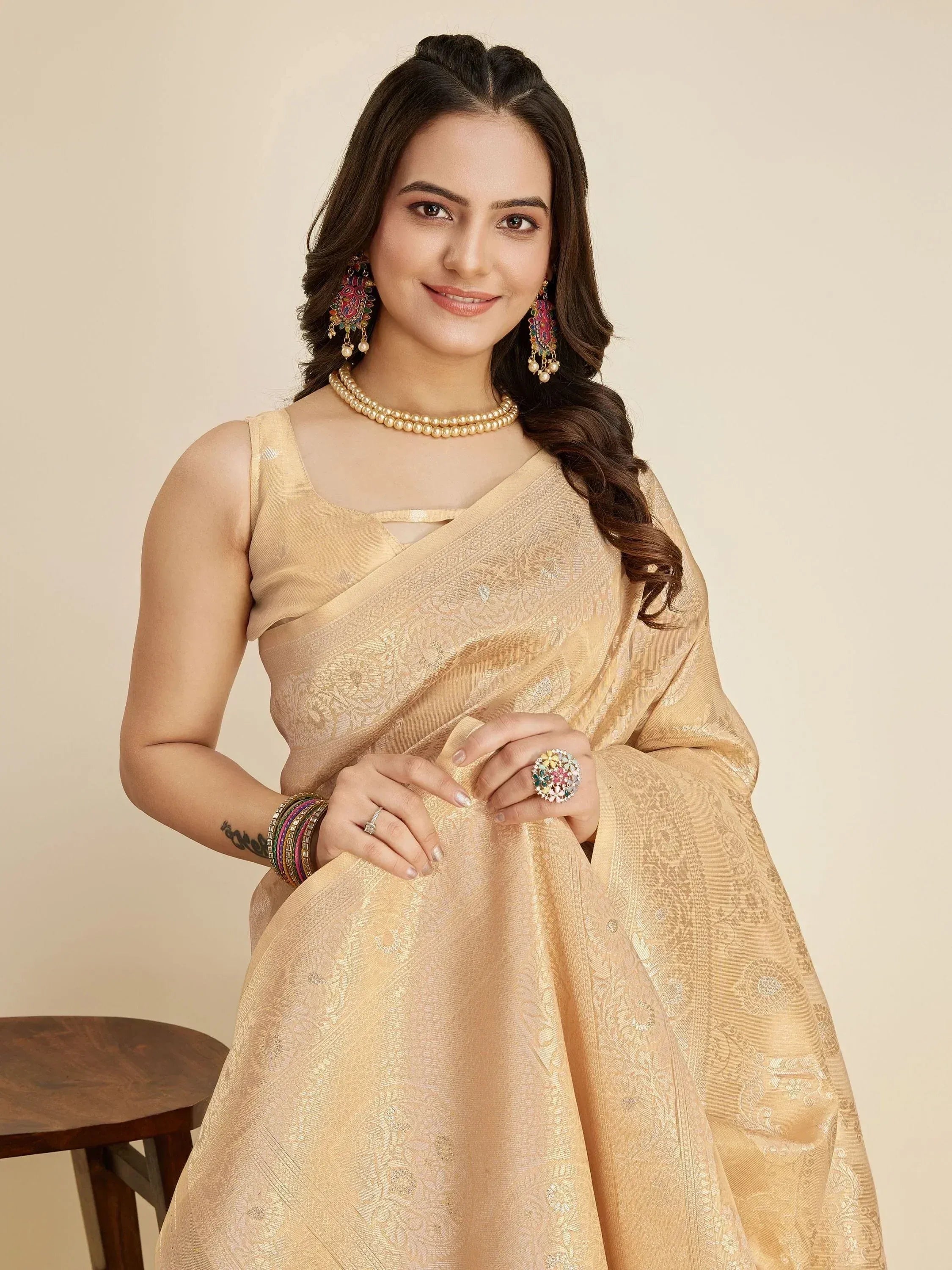 Woman in elegant gold designer saree with intricate floral patterns, paired with pearl necklace and colorful jhumka earrings.