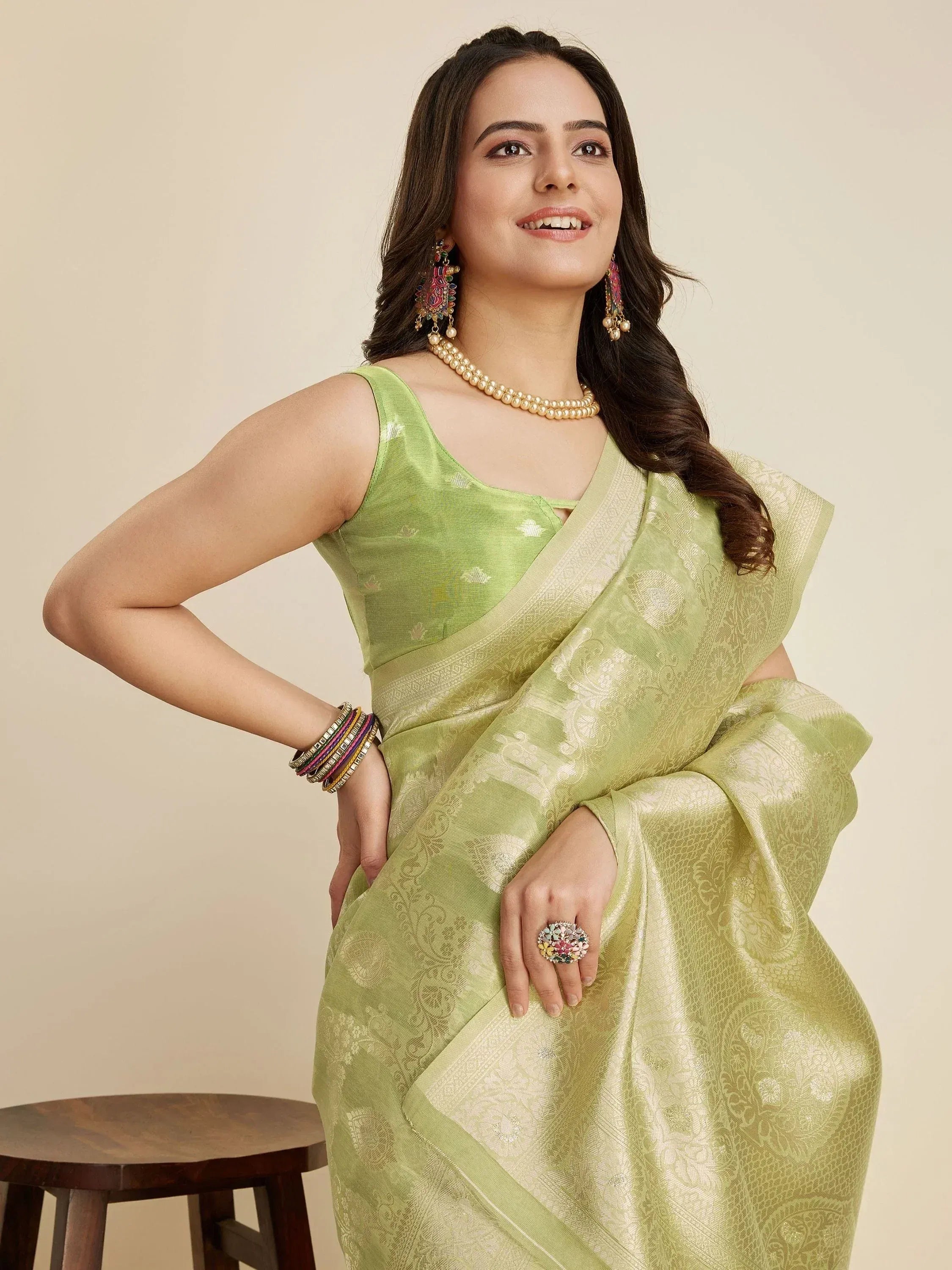 Woman in light green designer saree with gold embroidery, paired with pearl necklace and colorful jewelry