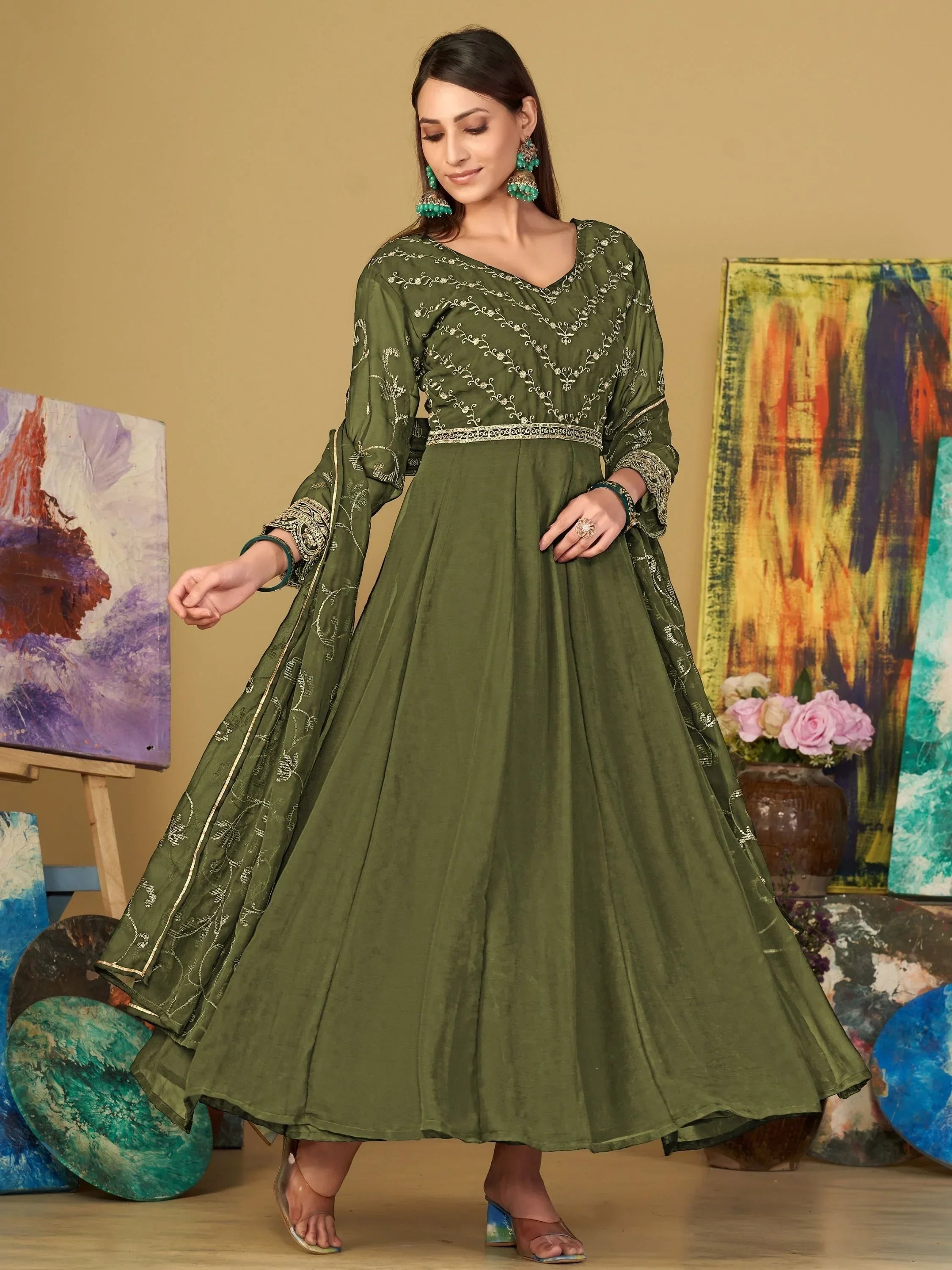 Woman wearing olive green embroidered ethnic gown with dupatta standing indoors