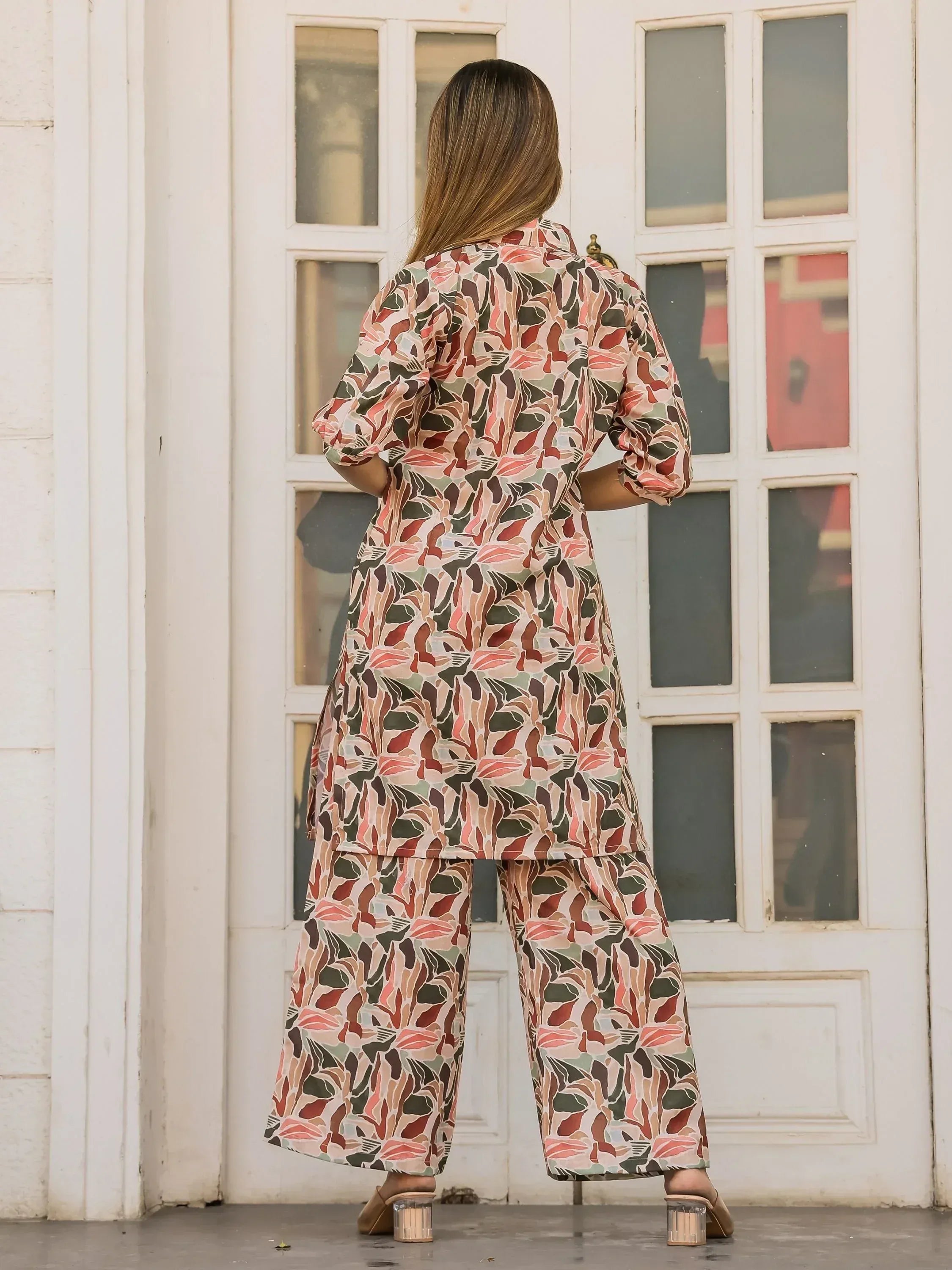 Woman in floral print ethnic kurta set with wide pants, back view near white door