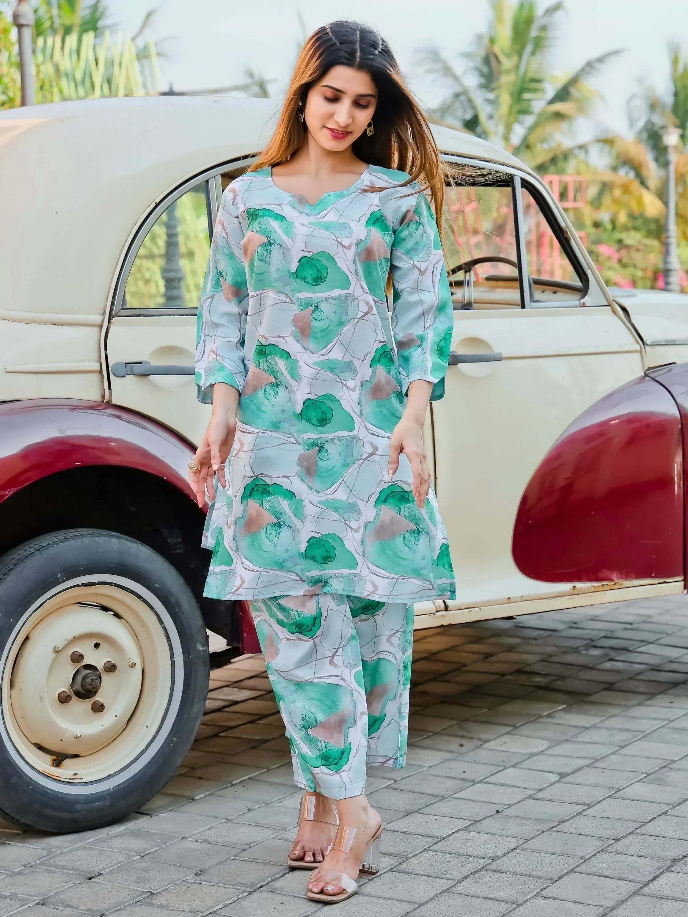 Woman in floral print kurta set with green and beige patterns, standing by vintage car outdoors