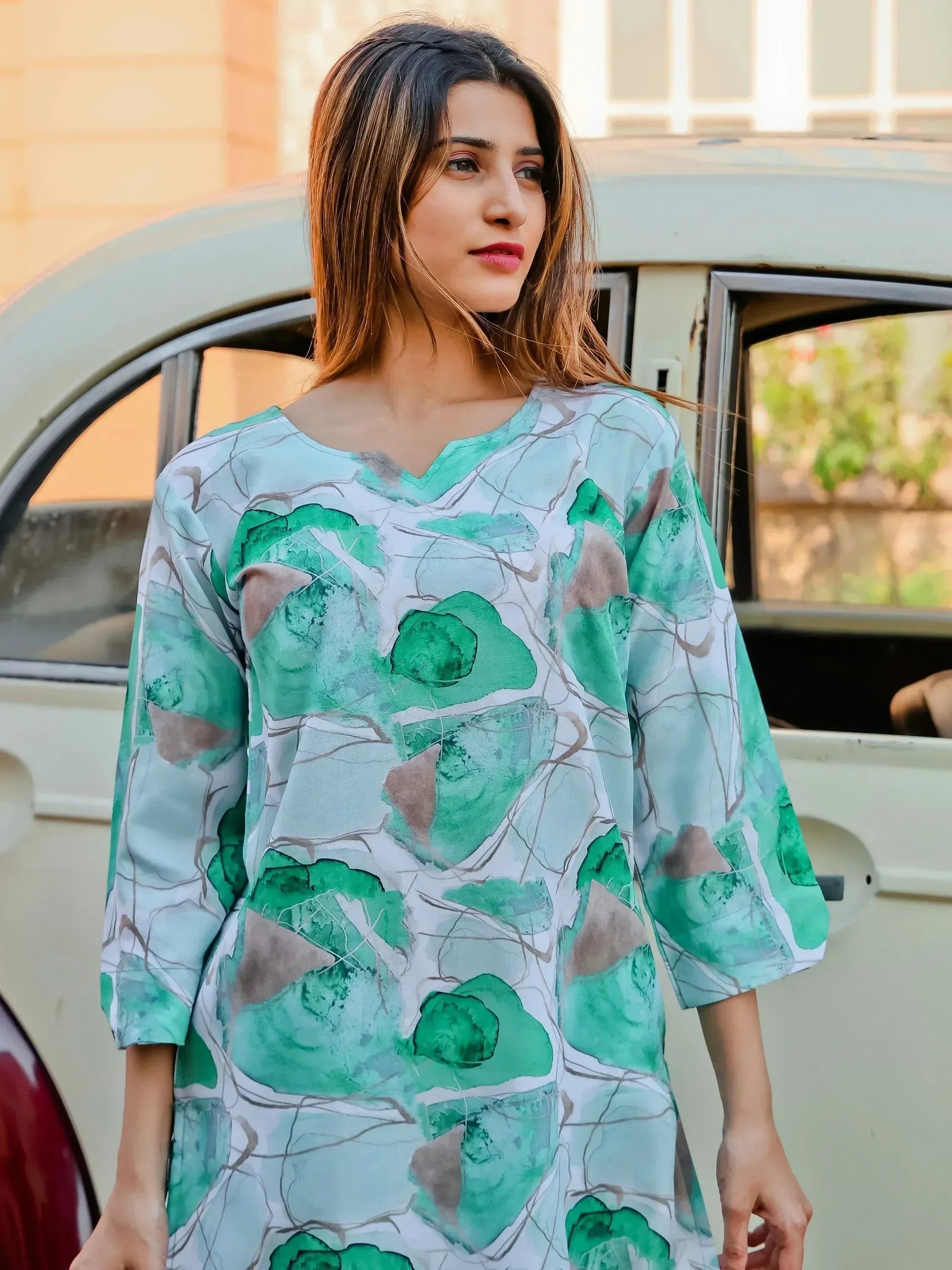 Woman in a green and white printed kurti standing outdoors by a vintage car