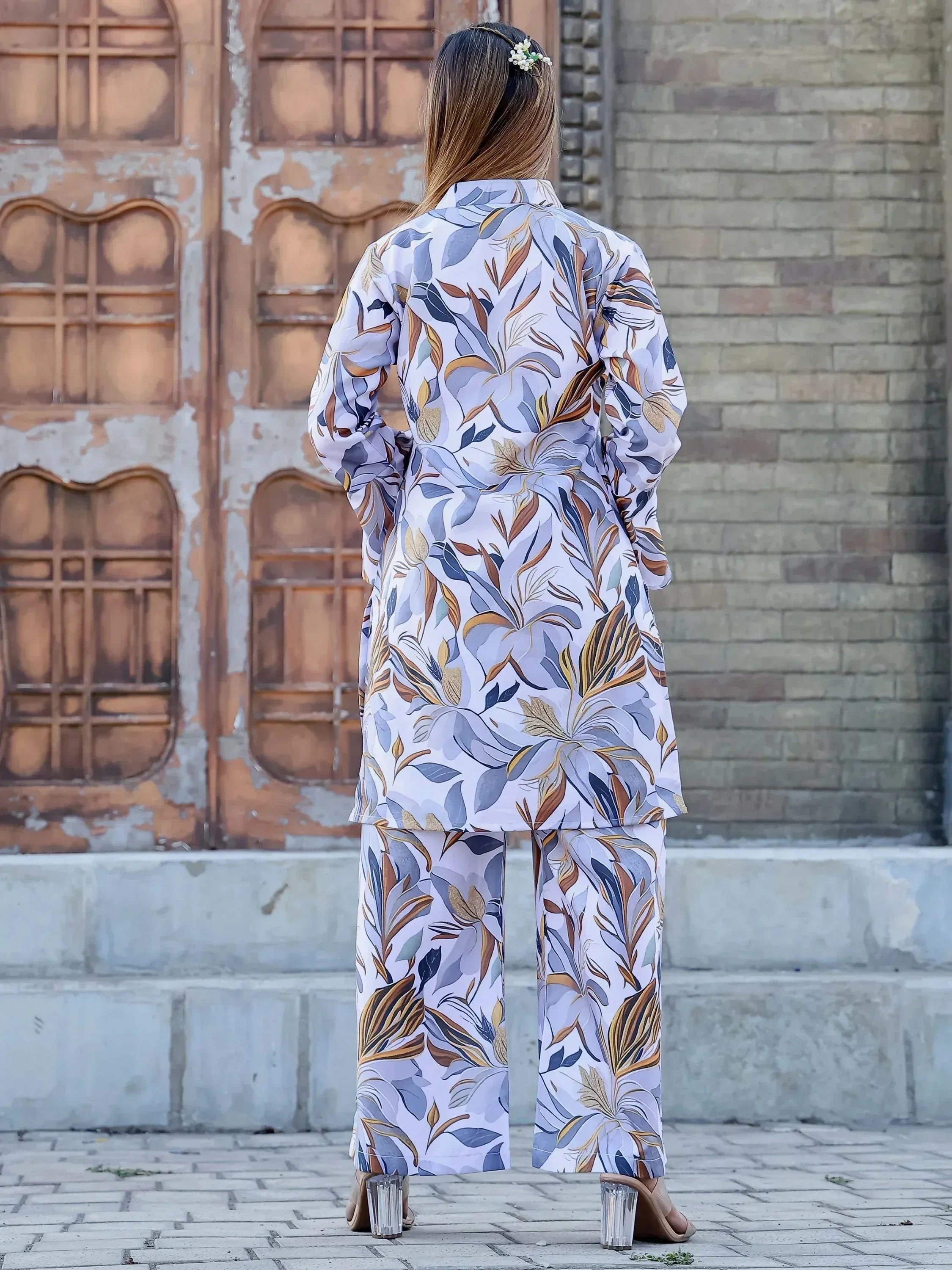 Woman in floral print salwar kameez with wide pants, back view, standing near rustic door