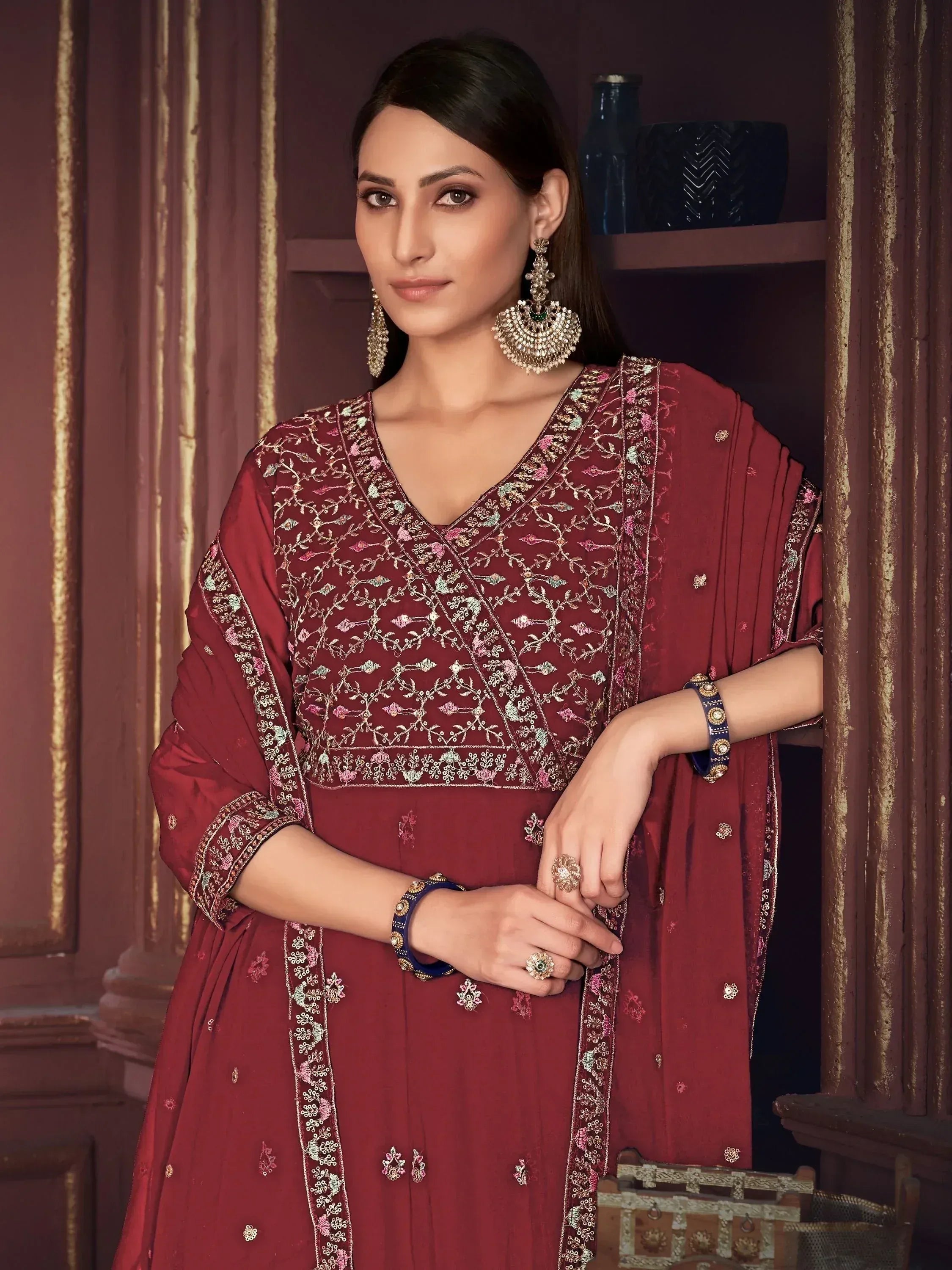 Maroon embroidered ethnic gown with floral detailing, paired with statement jewelry for festive occasions.