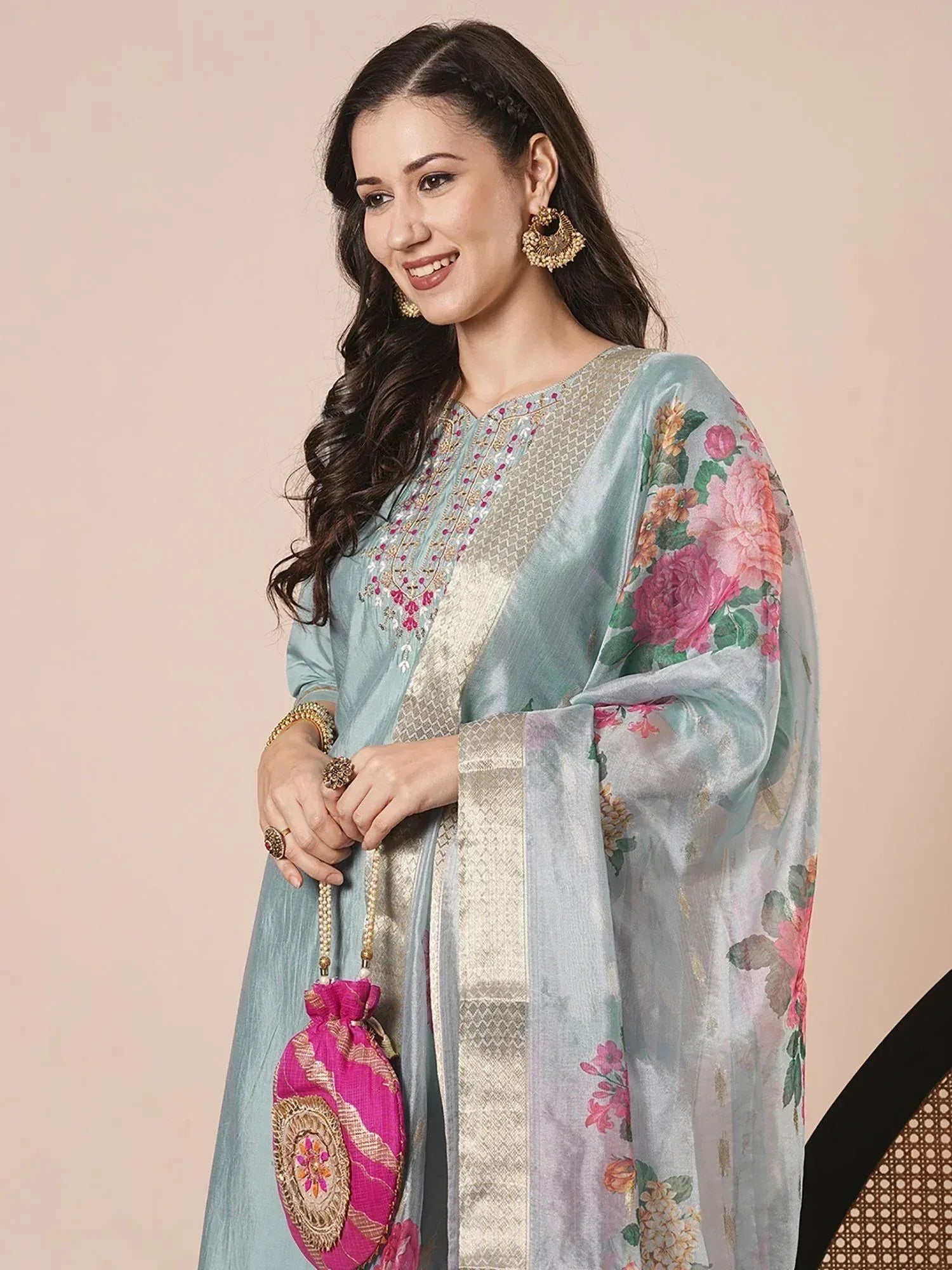 Woman in light blue floral printed salwar kameez with gold embroidery and pink potli bag