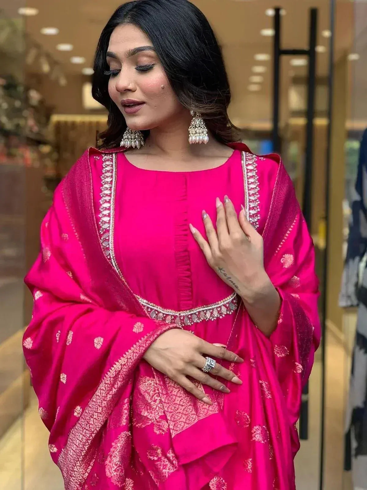Woman in vibrant pink ethnic gown with gold embroidery, paired with statement jhumka earrings for festive occasions.