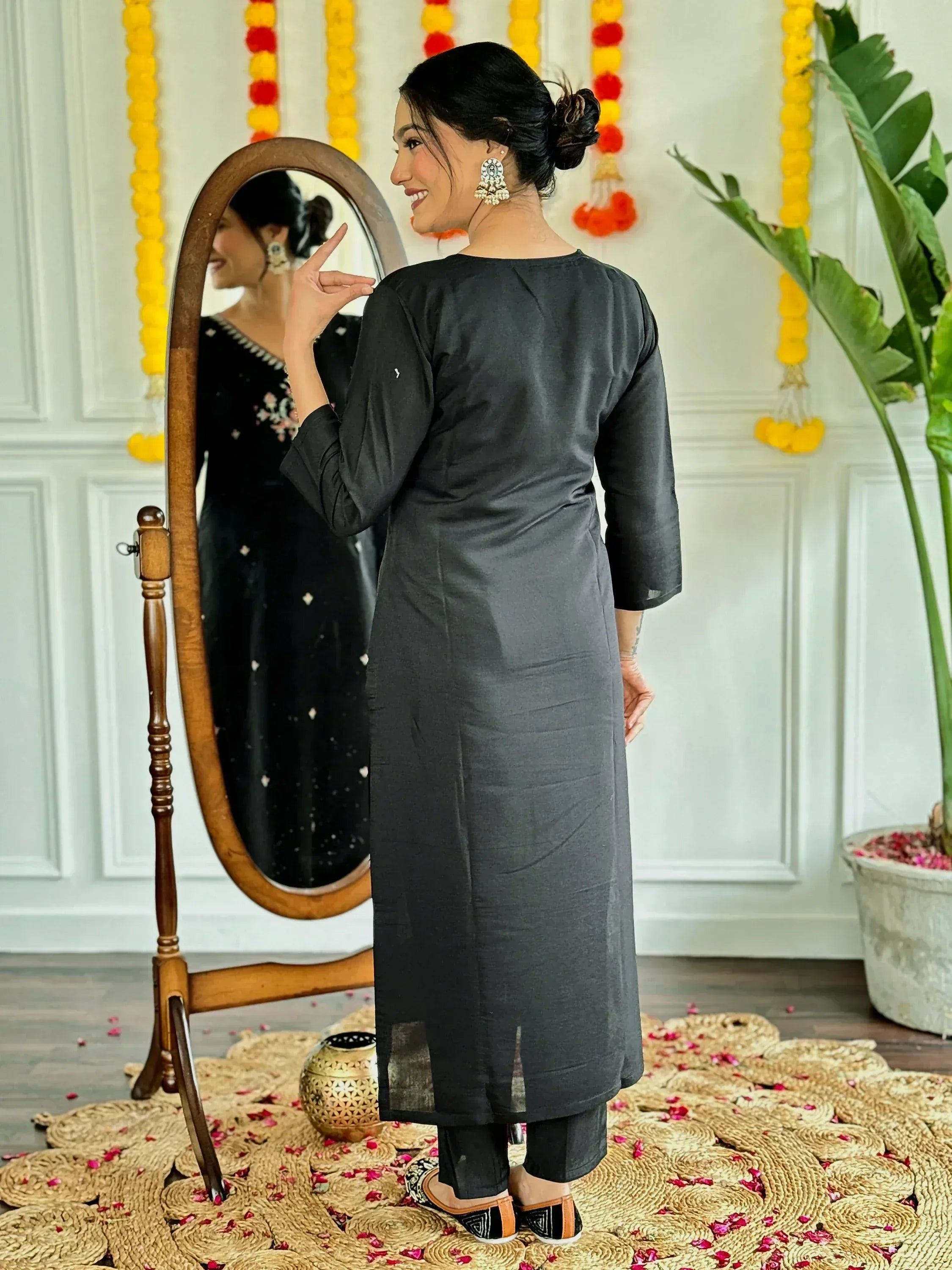 Woman in black ethnic kurta with mirror reflection, floral garlands, and traditional Indian decor