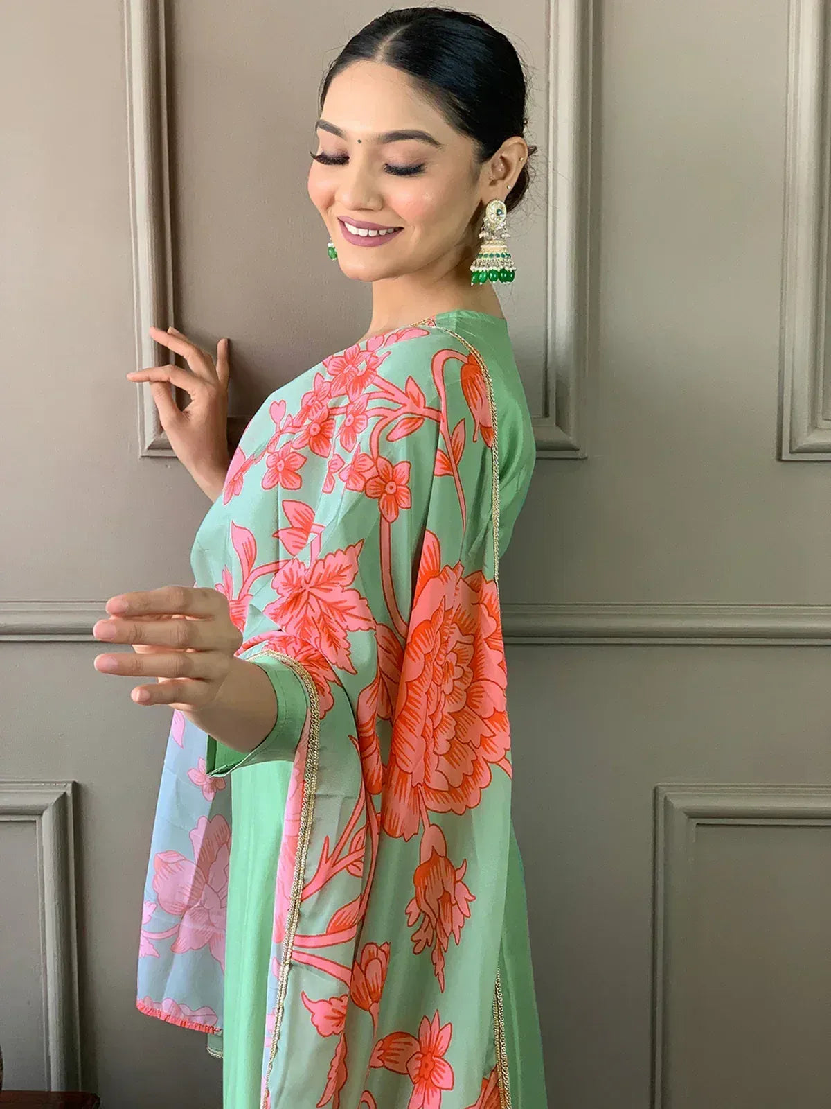 Woman in mint green floral printed ethnic gown with gold trim, paired with green jhumka earrings