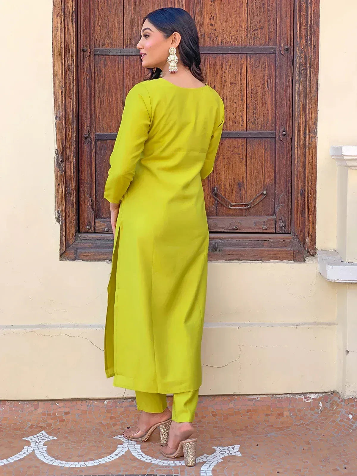 Lime green ethnic kurta set with side slit, paired with matching pants and gold heels, perfect for Indian occasions.