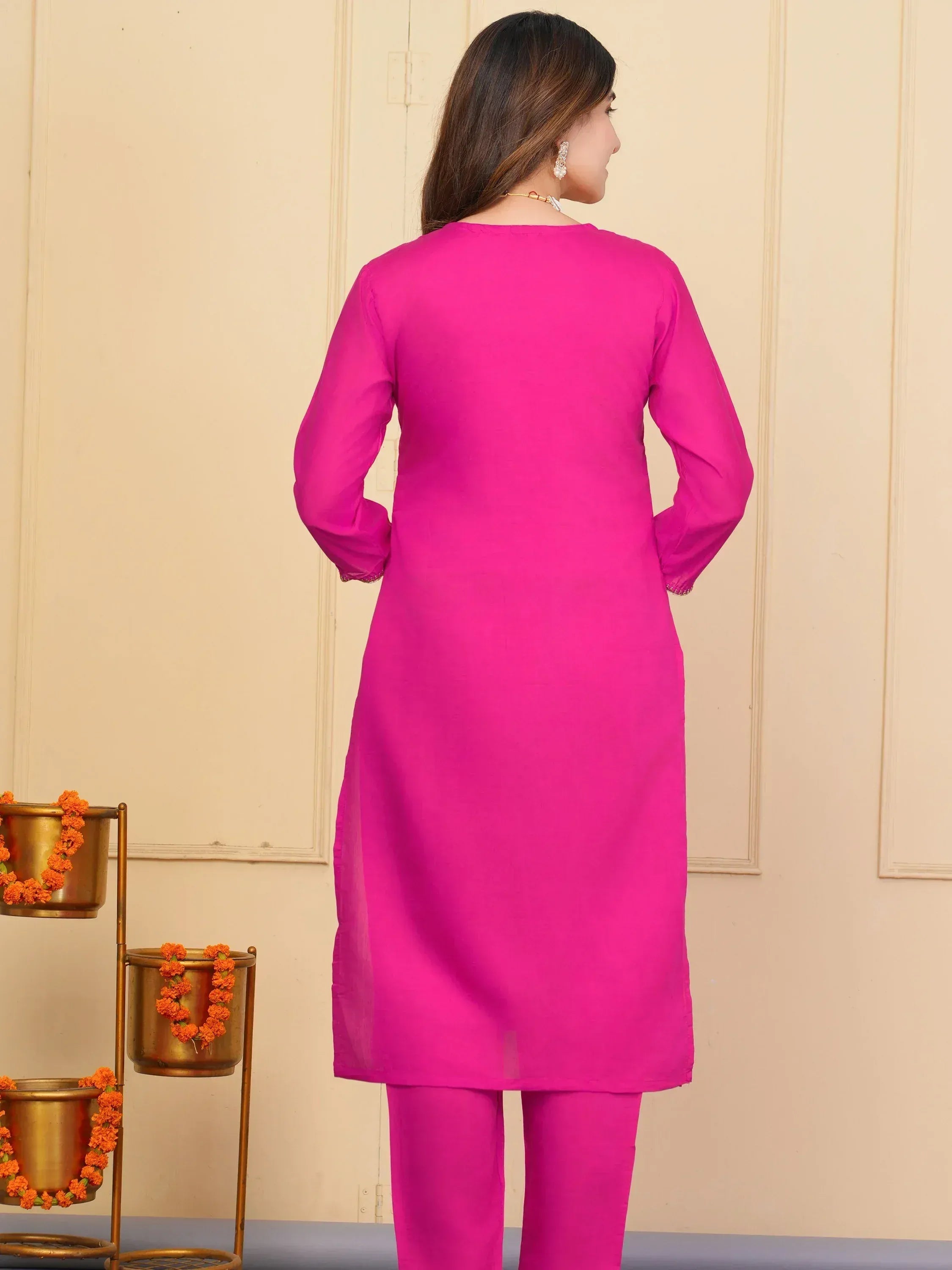 Vibrant pink ethnic kurta with matching pants, showcased in a traditional Indian setting with floral decor.