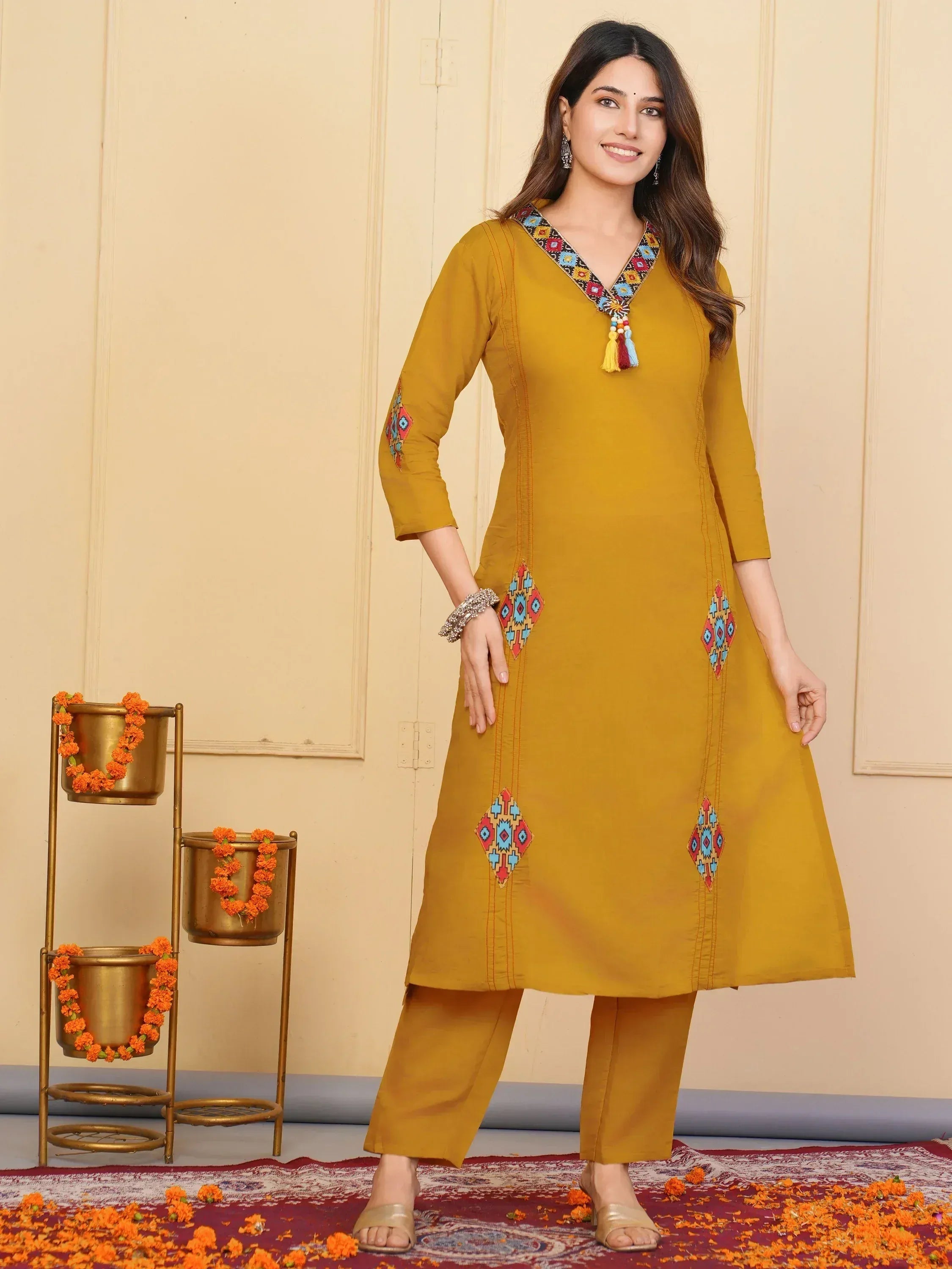 Mustard yellow ethnic kurti with colorful geometric embroidery and tassels, paired with matching pants for festive occasions